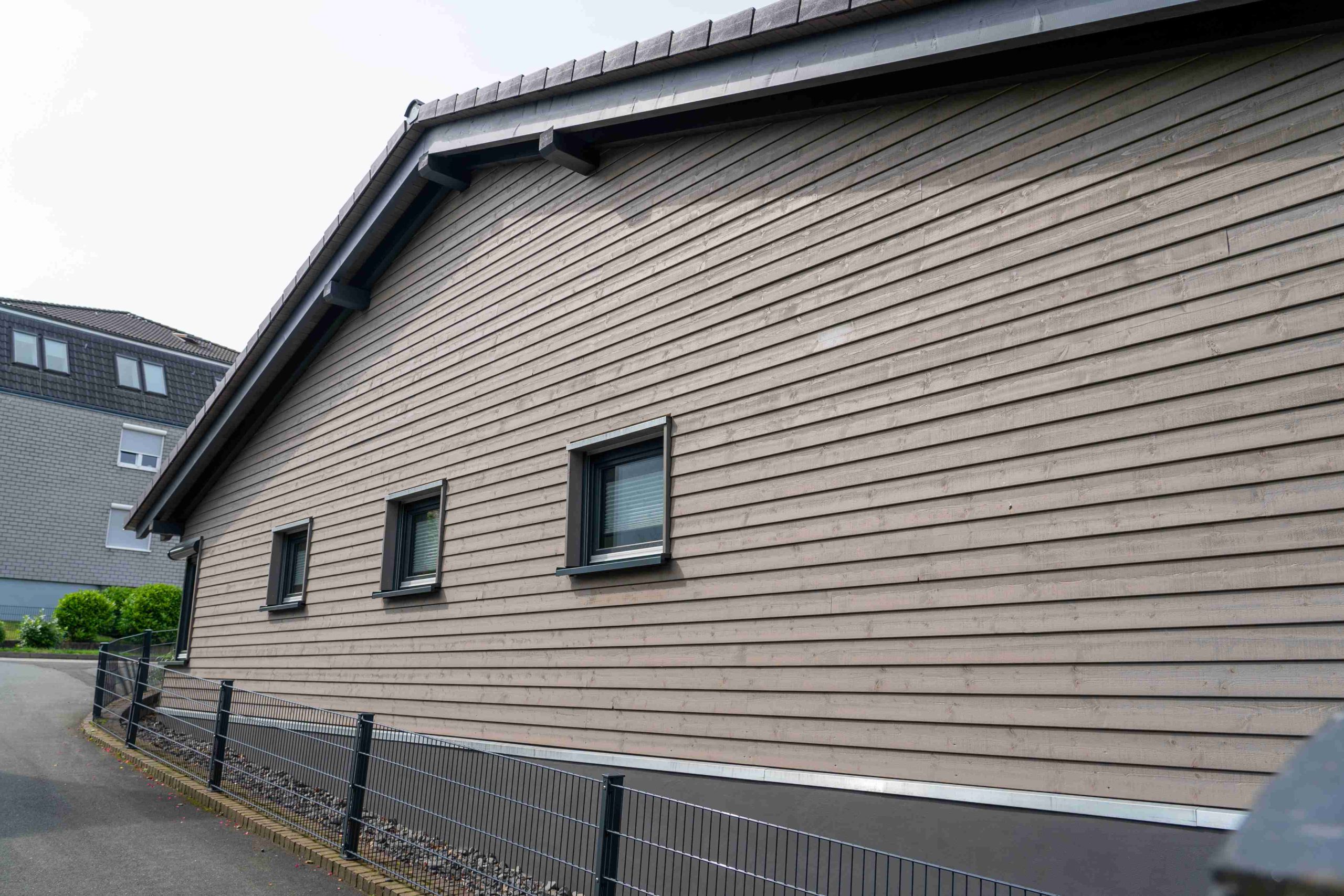 Seitenansicht der grauen Holzfassade mit drei Fenstern und Satteldach