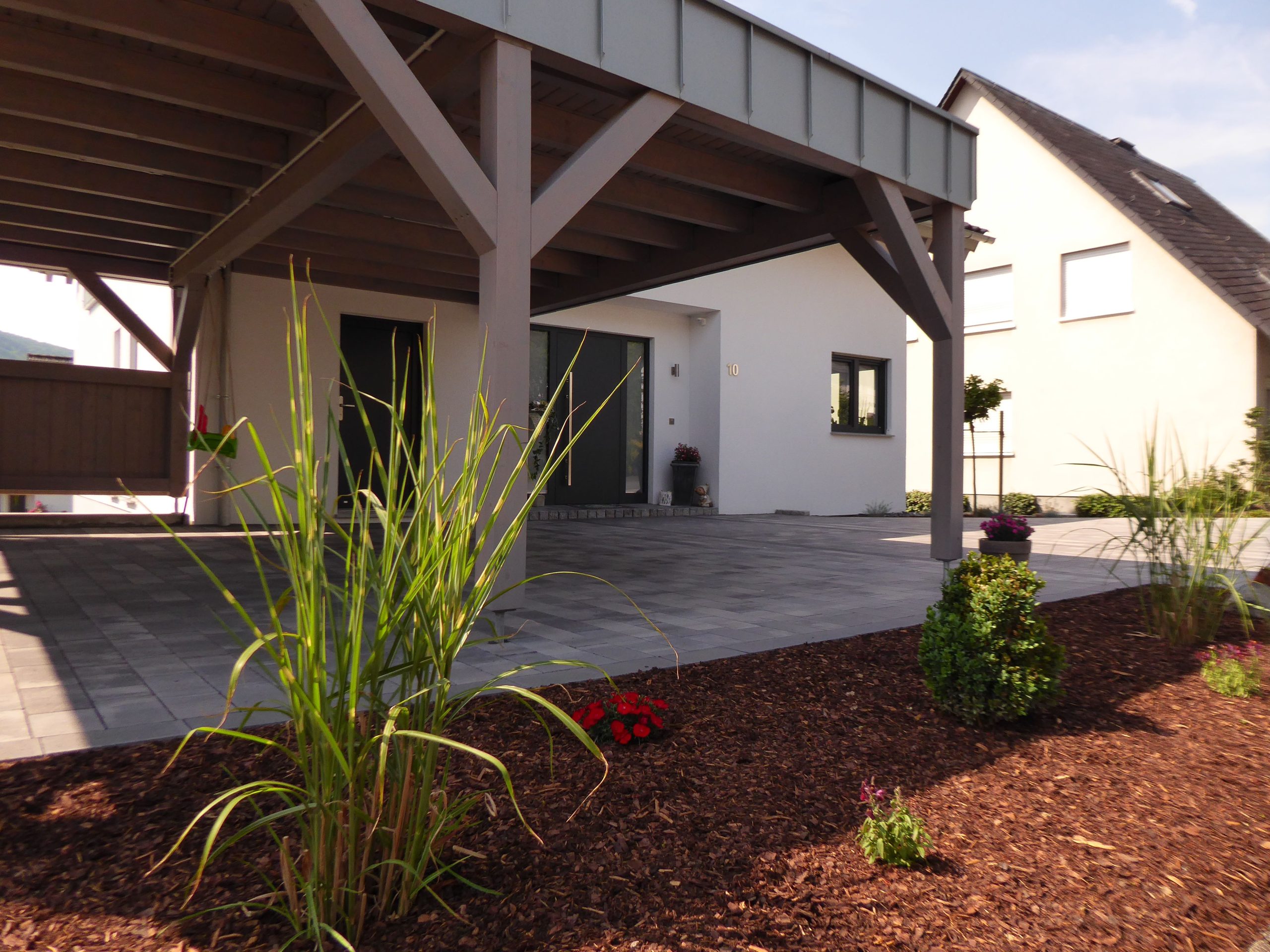 Ansicht des Carports und des Hauseingangs von Haus Vollmer mit Pflasterfläche und bepflanztem Vorgarten