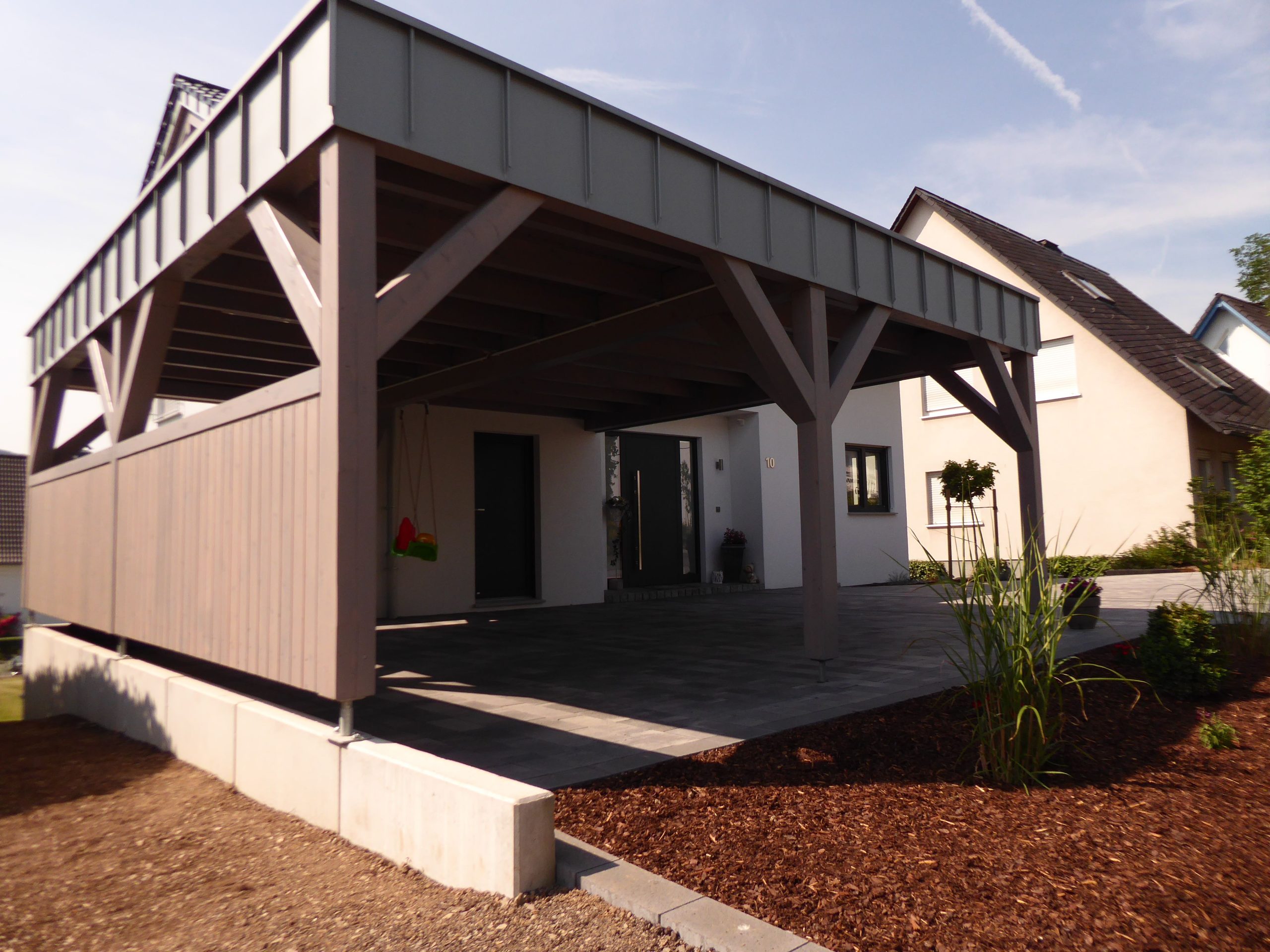 Seitliche Ansicht des Doppelcarports von Haus Vollmer mit Holzstützen und seitlichem Sichtschutz