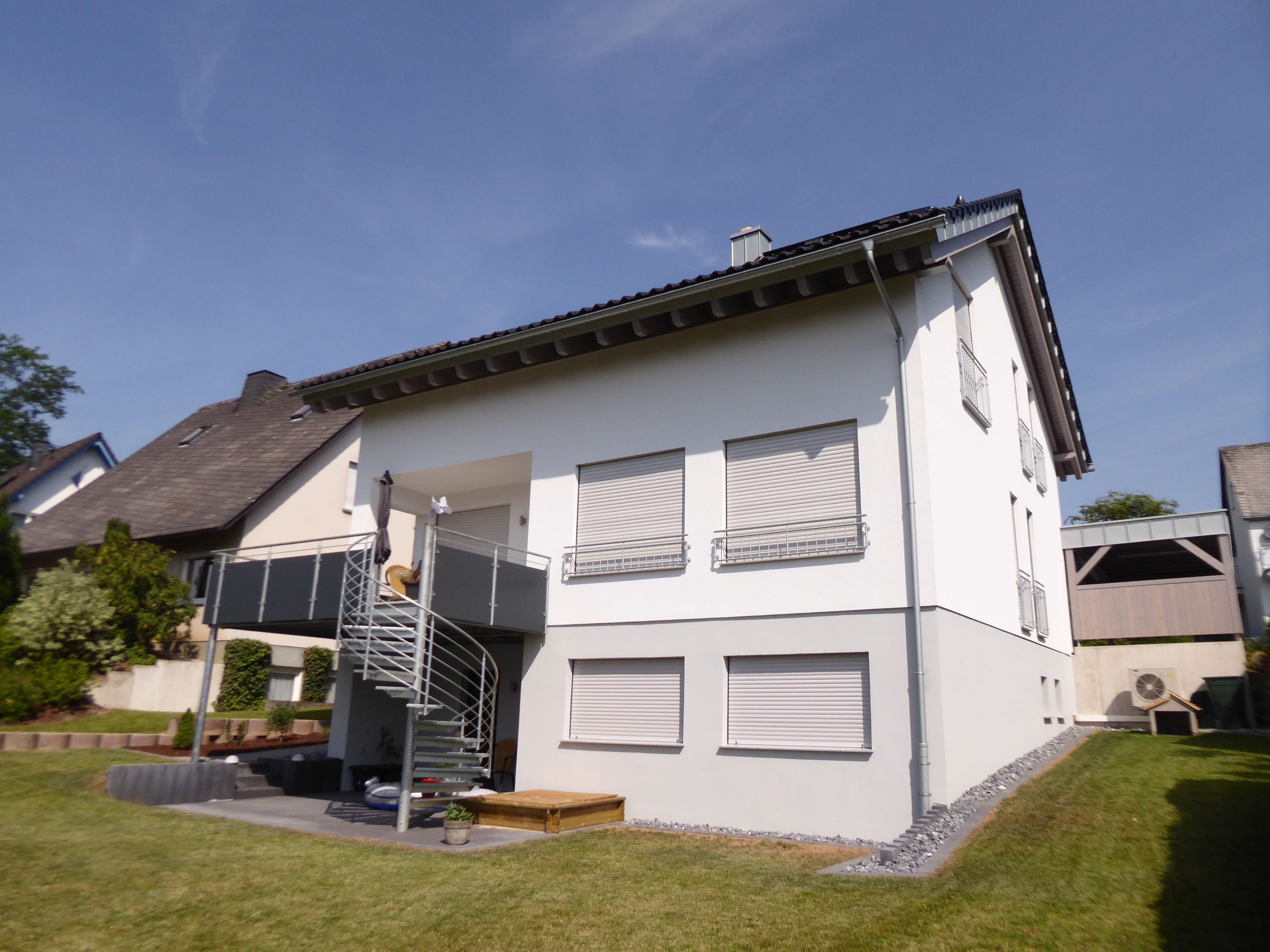 Rückansicht von Haus Vollmer mit überdachtem Südbalkon, Wendeltreppe zum Garten und Terrasse im Untergeschoss