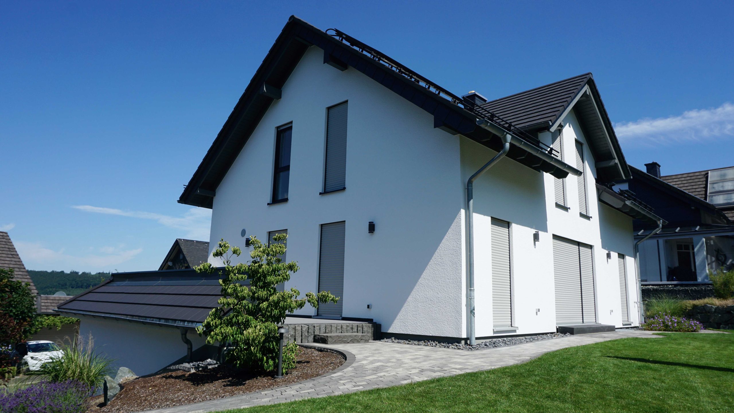 Außenansicht des Einfamilienhauses am Hang mit Doppelgarage, terrassiertem Grundstück und weißer Putzfassade