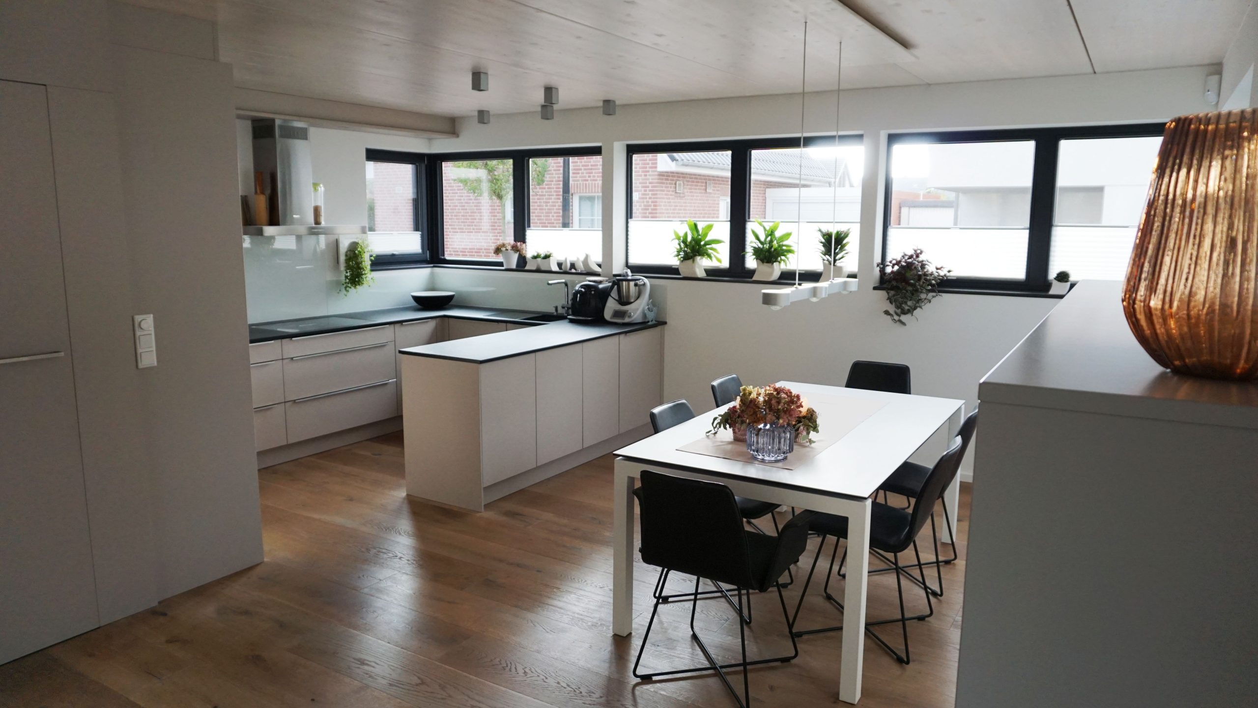 Moderner Küchen- und Essbereich mit großem Fensterband, Einbaumöbeln und Holzboden