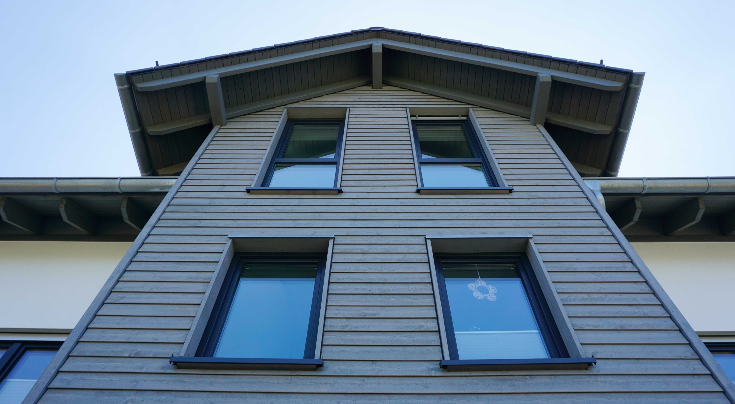 Nahaufnahme der grauen Holzfassade des Erkers mit drei übereinanderliegenden Fenstern