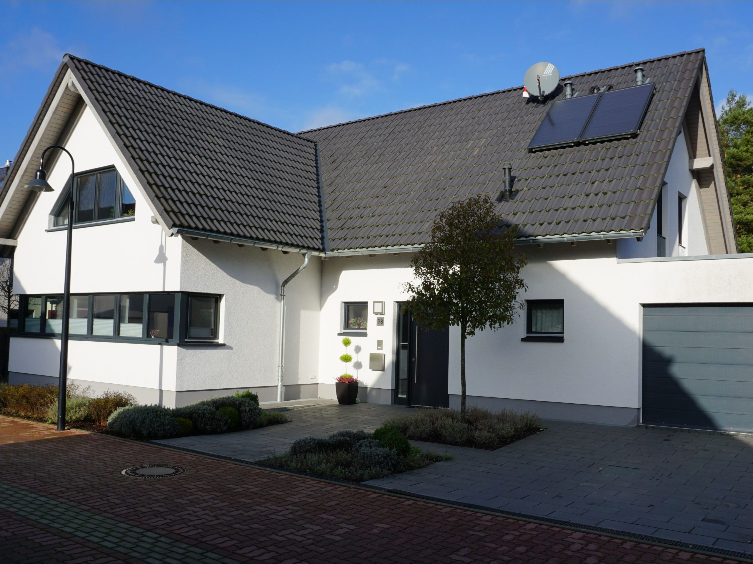 Eingangsbereich des Wohnhauses mit vorgelagertem Baum, Garage und dunklem Satteldach