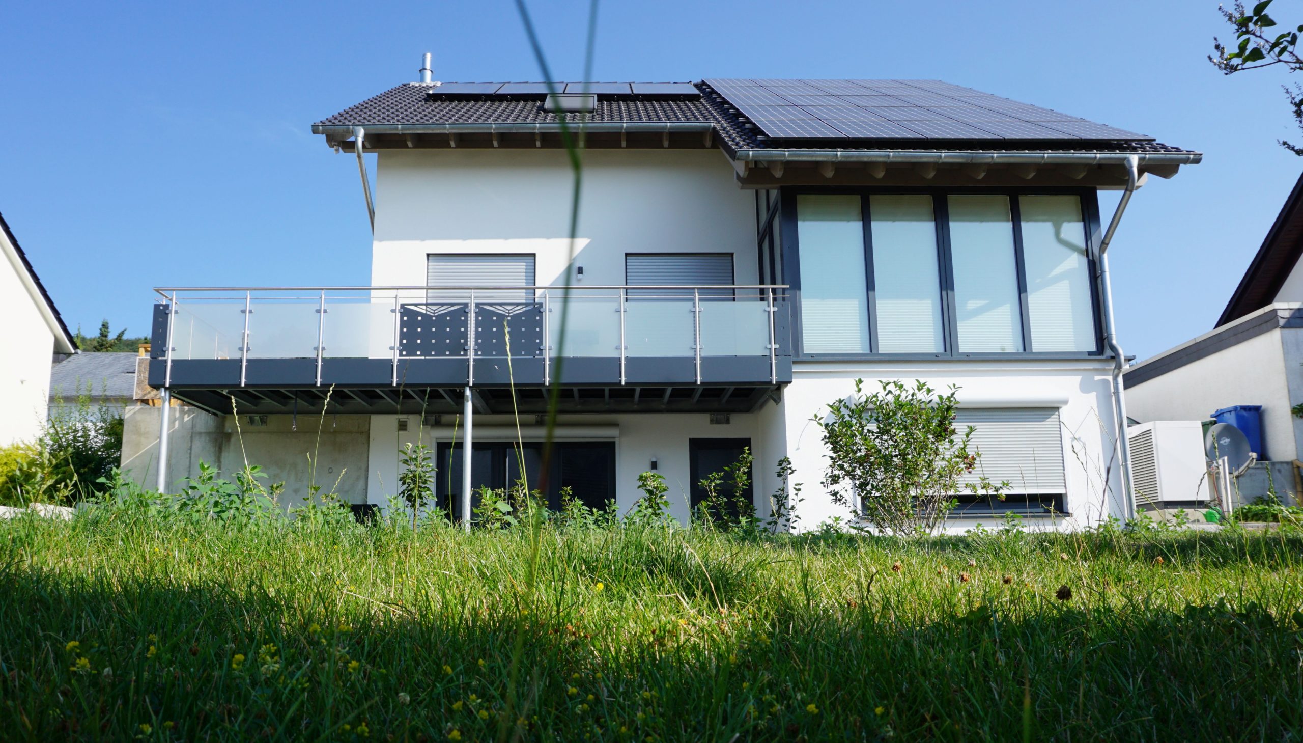 Gartenseitige Ansicht des EInfamilienhauses mit Balkon, großen Fenstern und Hanglage