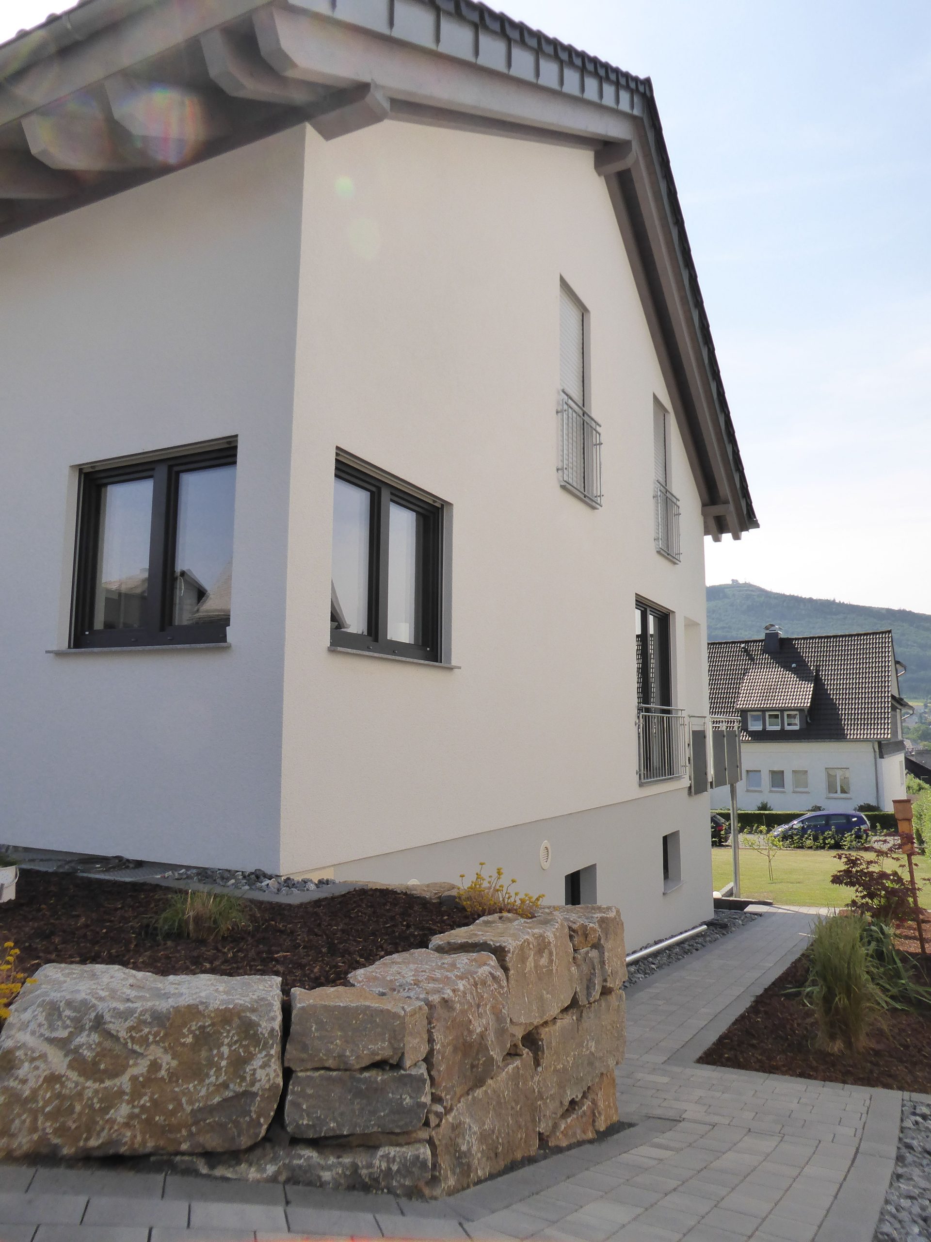 Seitenansicht von Haus Vollmer mit weißer Putzfassade, Fensterfront und vorgelagerter Natursteinmauer im Eingangsbereich