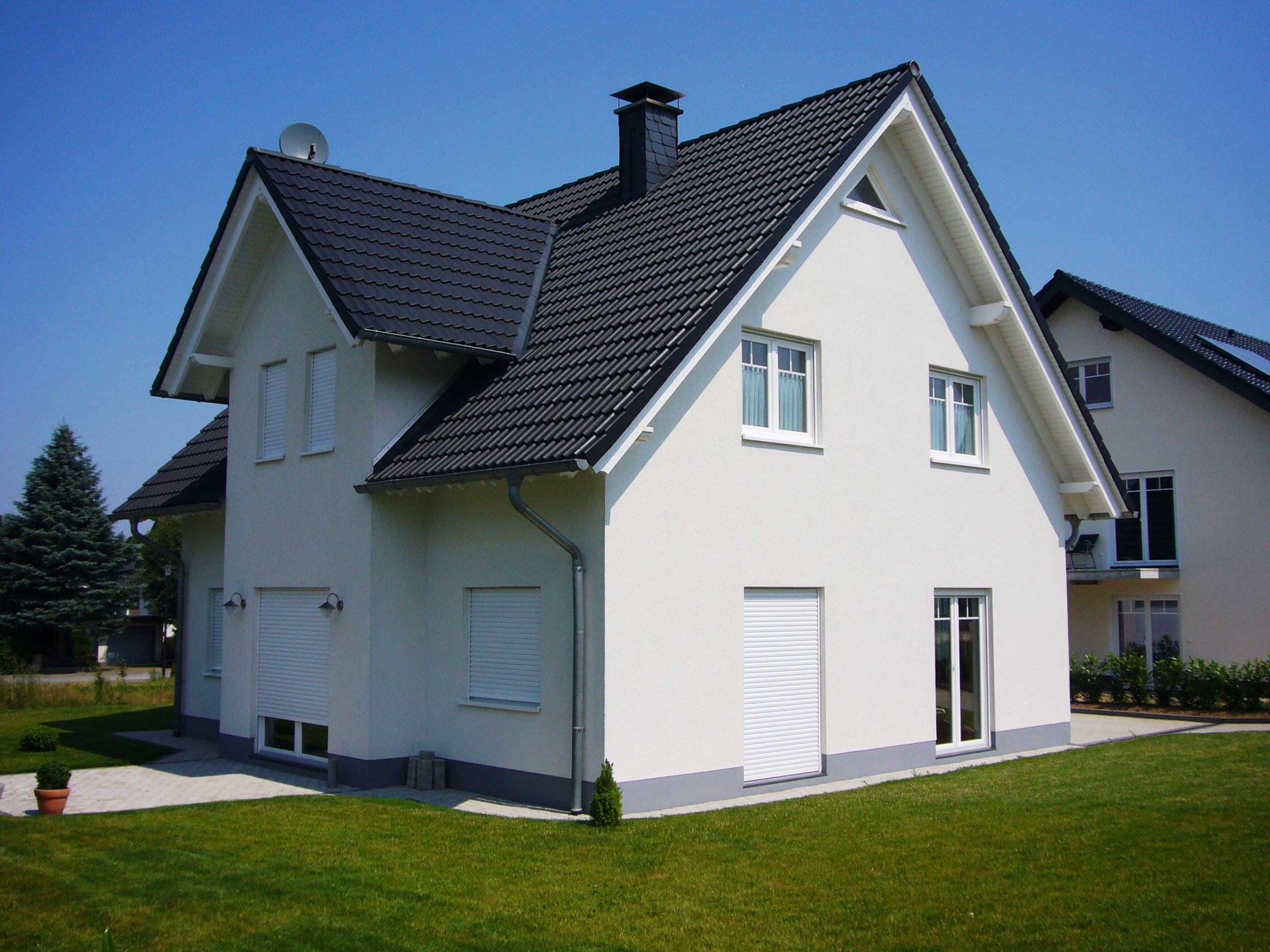 Südansicht des Einfamilienhauses mit weißer Putzfassade, Satteldach und Gartenbereich.