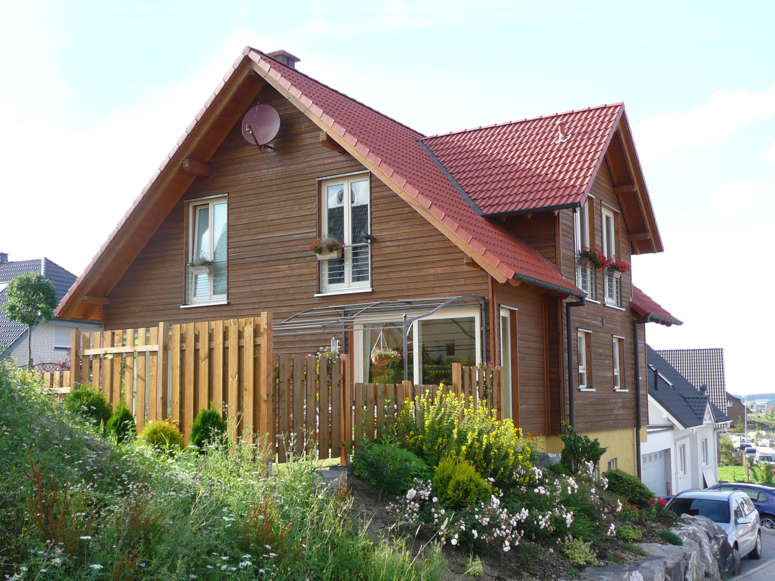 Gartenansicht des Holzhauses Asprion mit Zaun und Bepflanzung