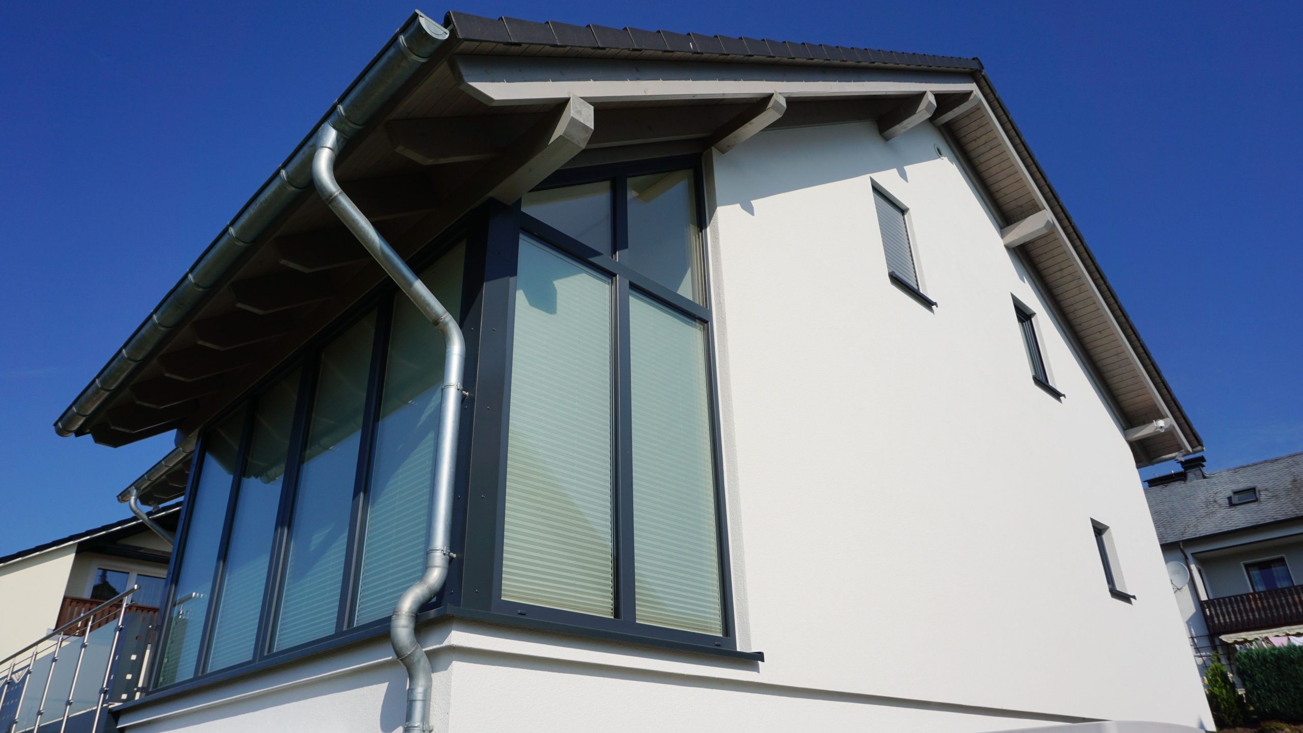 Fassadendetail des Hauses mit großflächiger Eckverglasung und anthrazitfarbenen Fensterrahmen