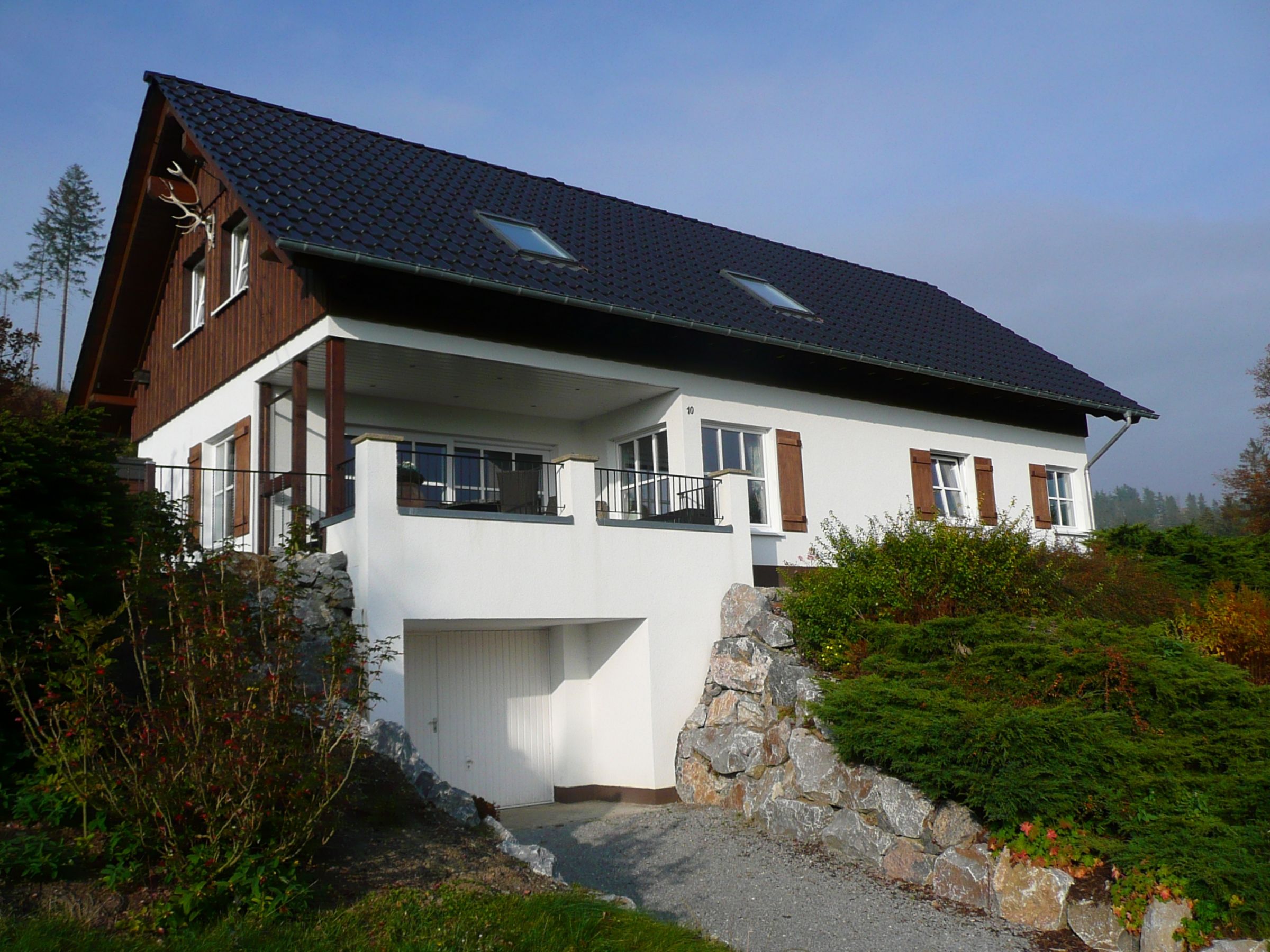 Hangseitige Ansicht eines Ferienhauses mit Balkon und Natursteinmauer