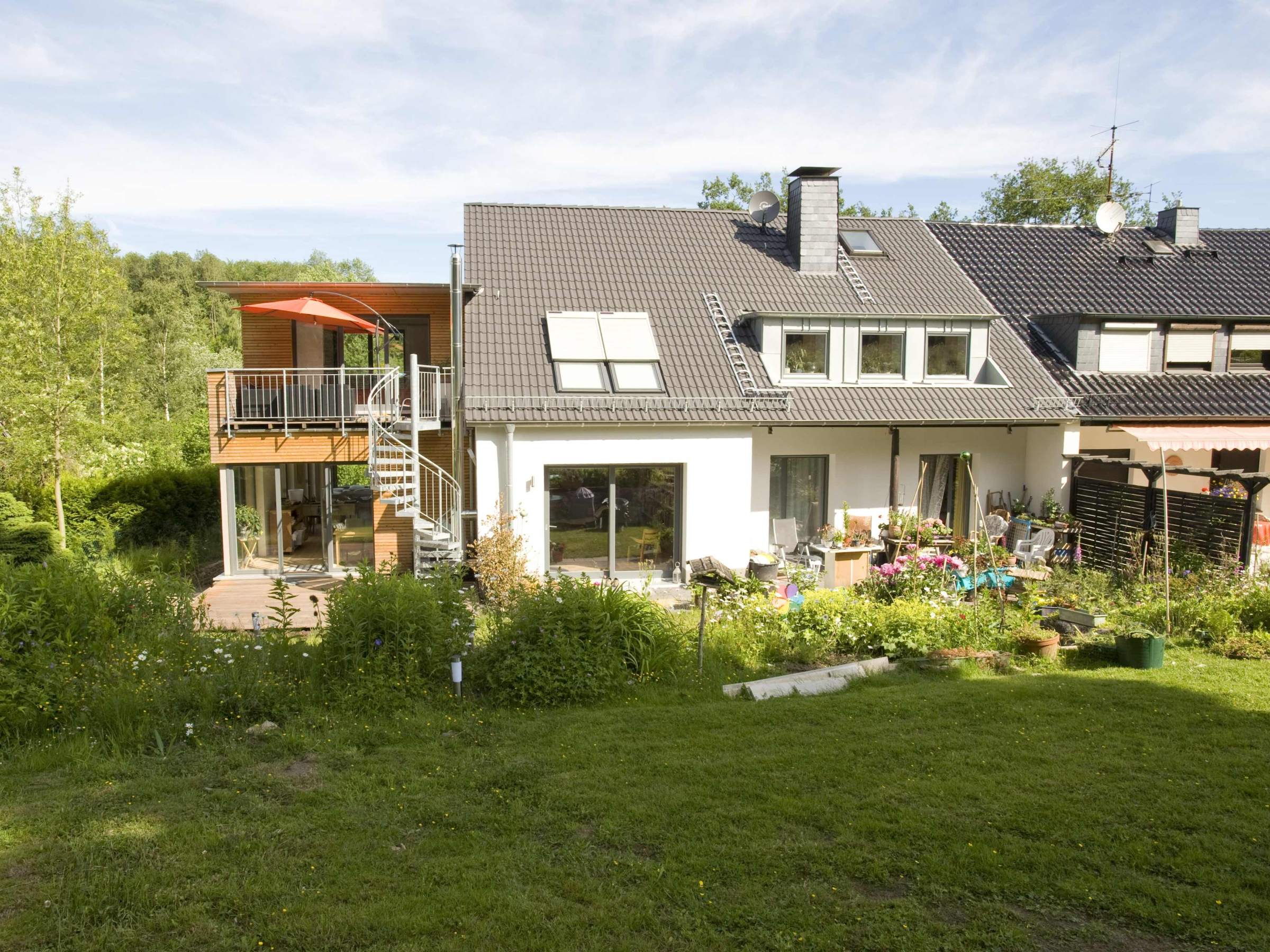 Rückansicht des Wohnhauses mit lichtdurchflutetem Holz-Anbau und Balkonen