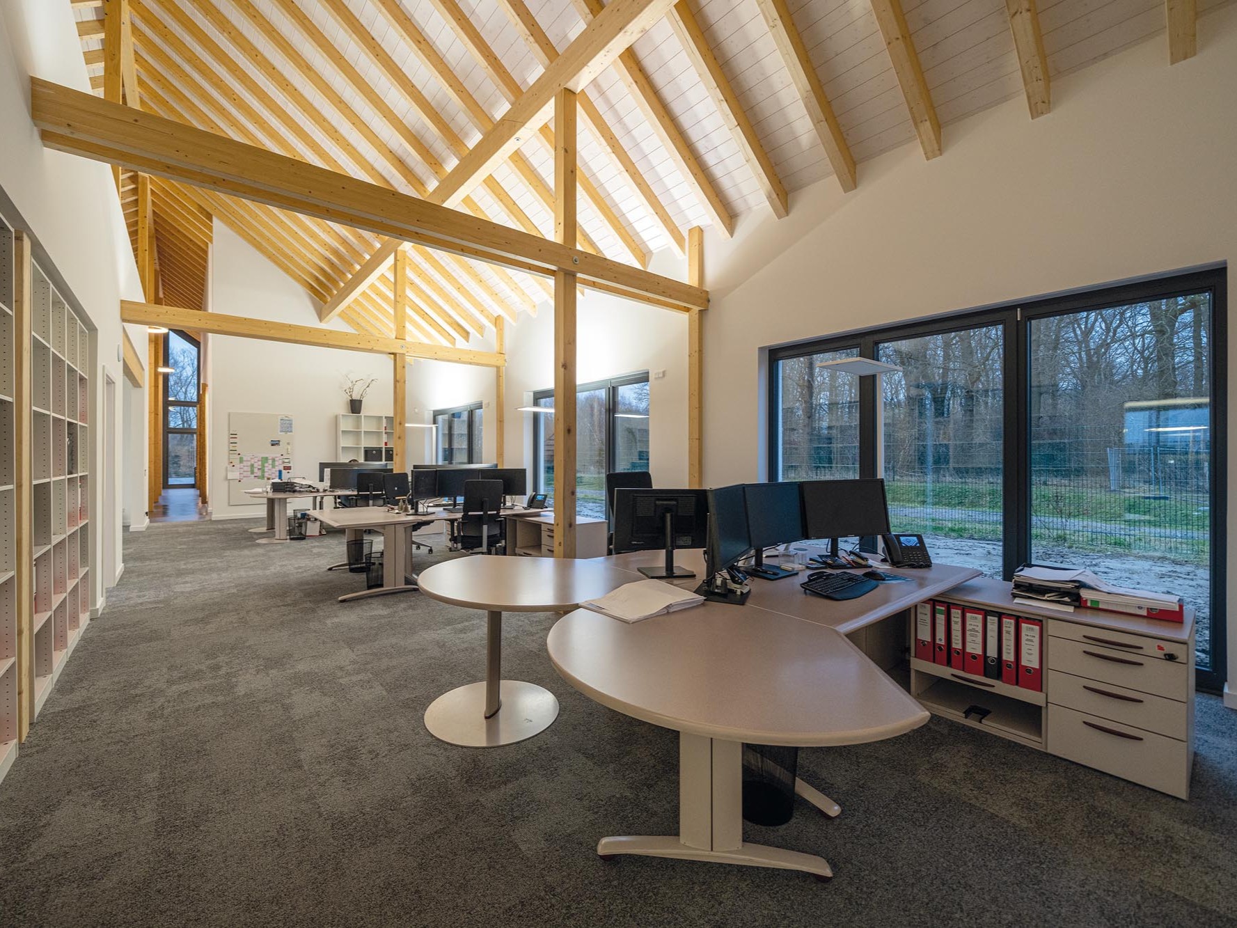 Großraumbüro mit Arbeitsplätzen, Holzstützen und offenem Dachstuhl in einem Bürogebäude in Holzbauweise