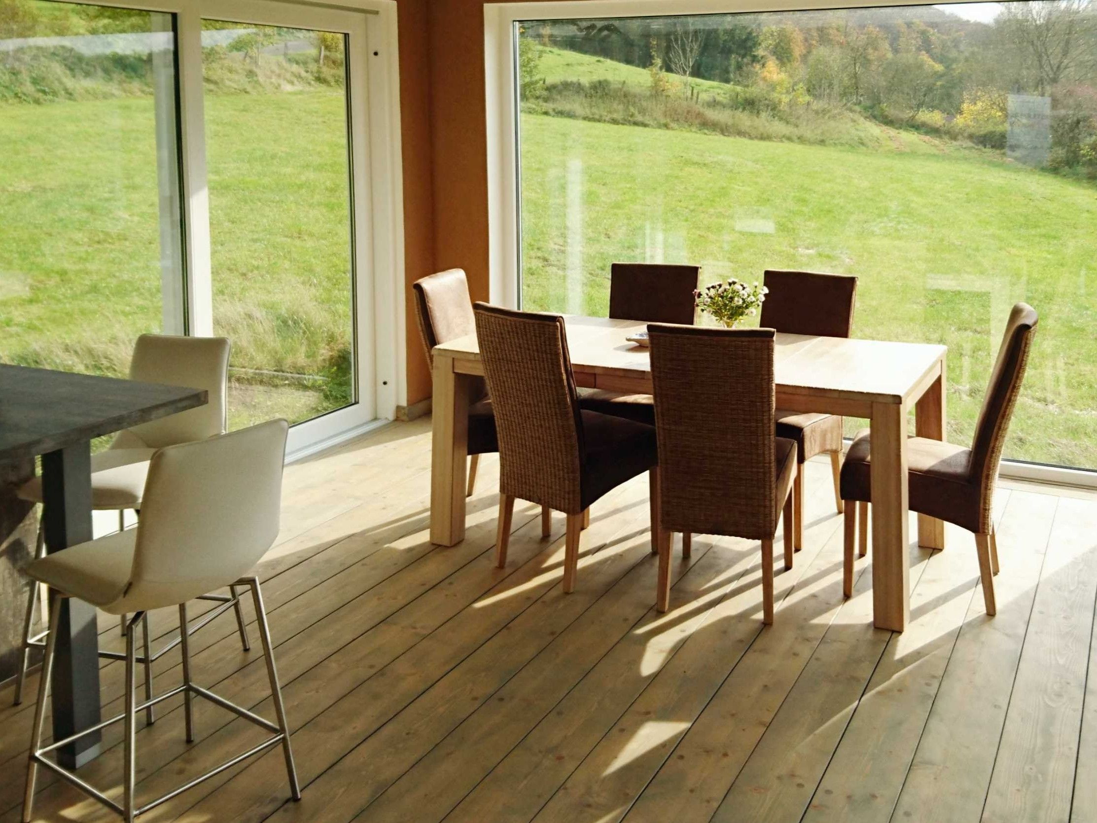Essbereich mit Holzboden und Esstisch vor bodentiefen Fenstern mit Ausblick auf die Wiese