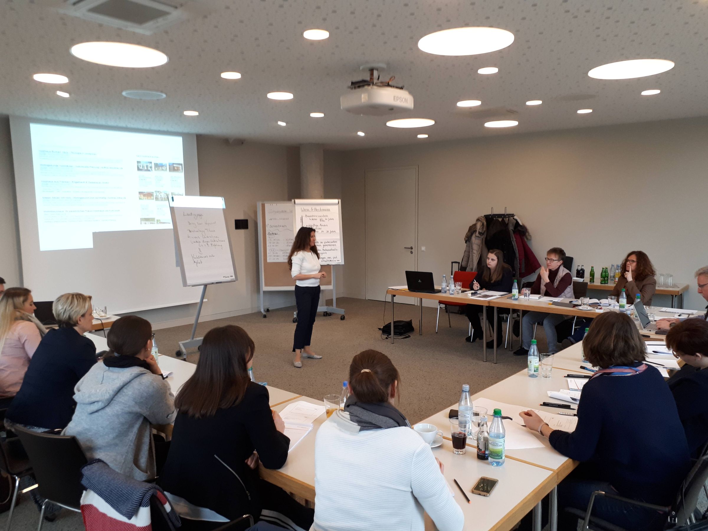 Teilnehmende eines Workshops sitzen an Tischen und verfolgen einen Vortrag in einem Seminarraum