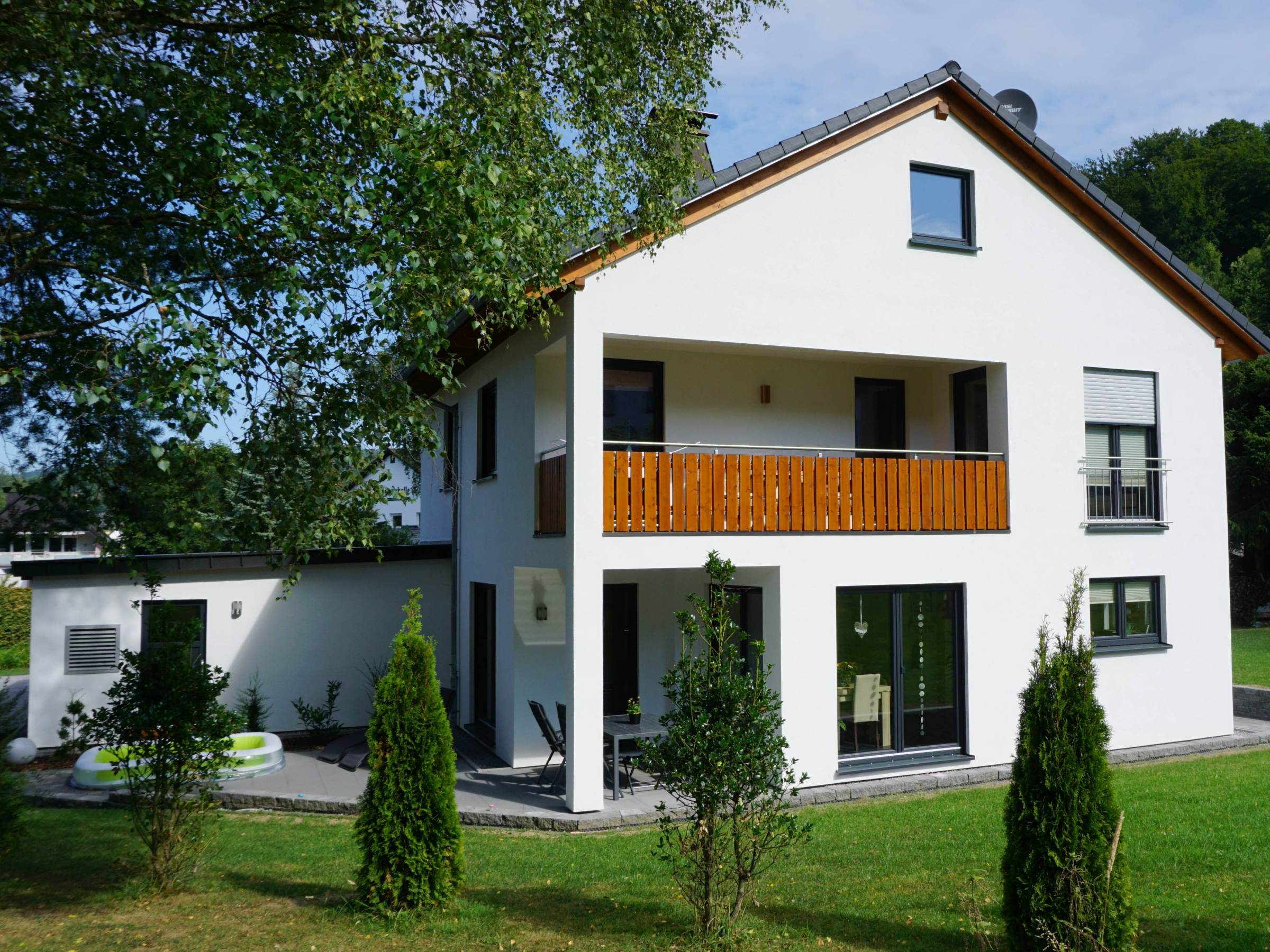 Detailansicht des Balkons mit vertikalem Holzgeländer und weißer Putzfassade