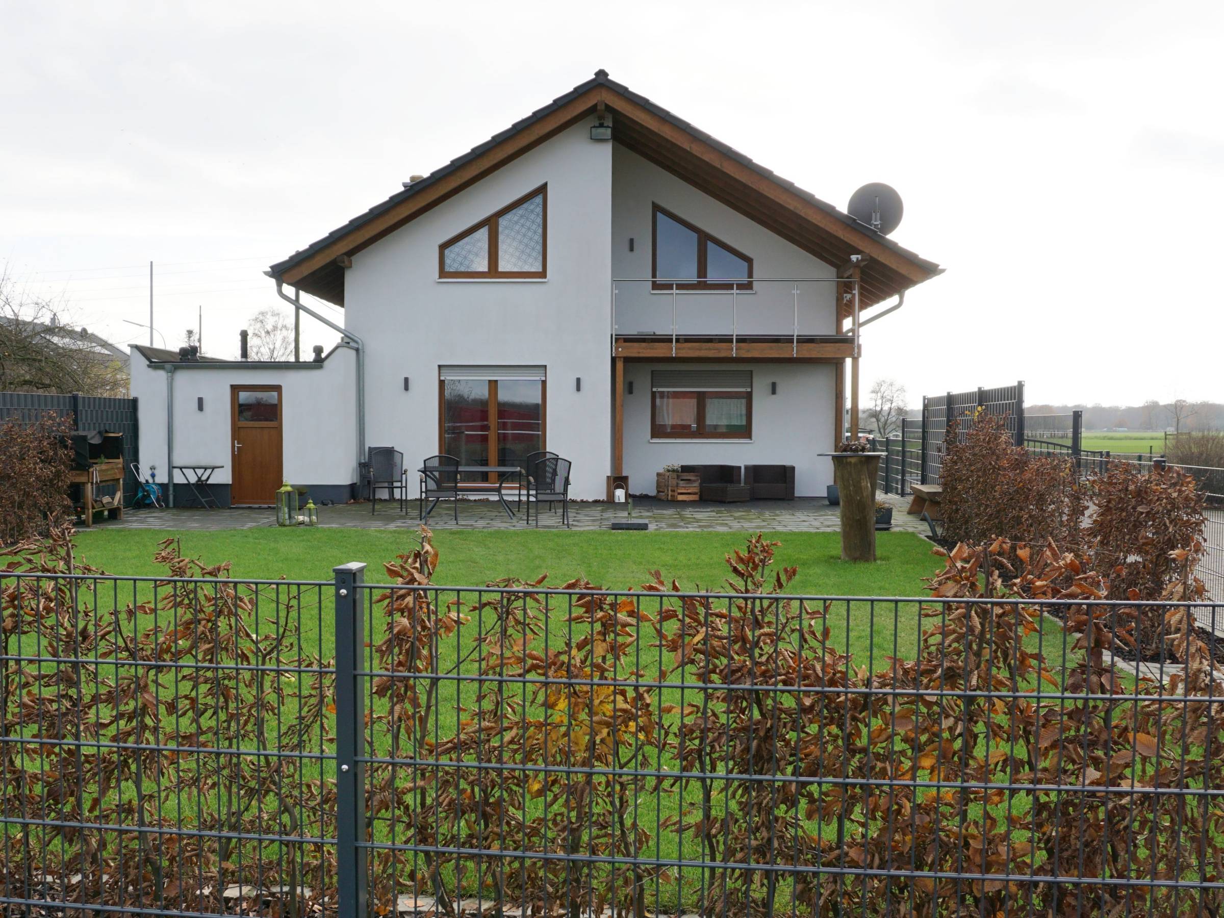 Gartenseite eines Einfamilienhauses mit Balkon, Terrasse und Rasenfläche