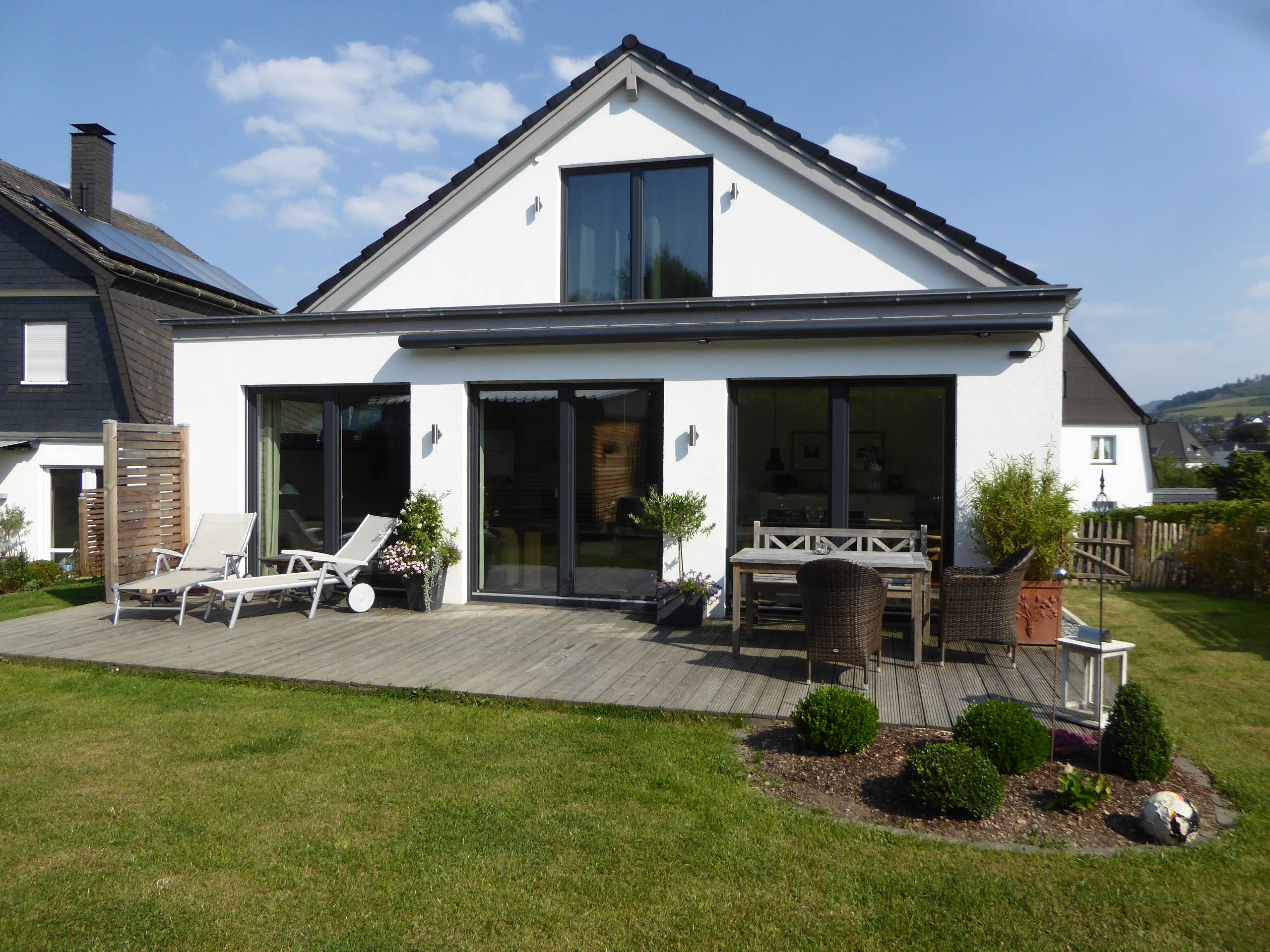 Außenansicht des Wohnhauses mit Terrasse, bodentiefen Fenstern und Blick in den Garten