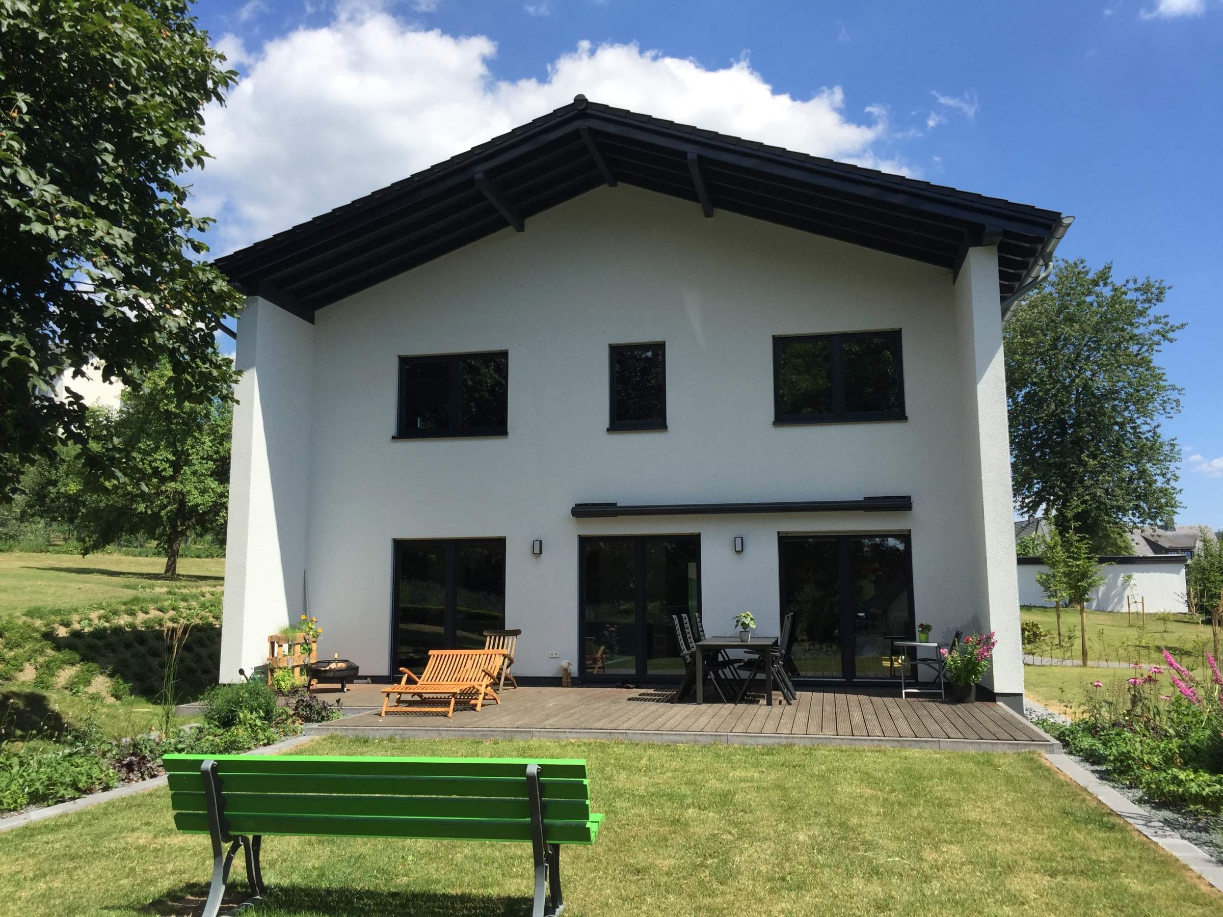 Gartenseitige Außenansicht eines Holzhauses mit Putzfassade und Terrasse