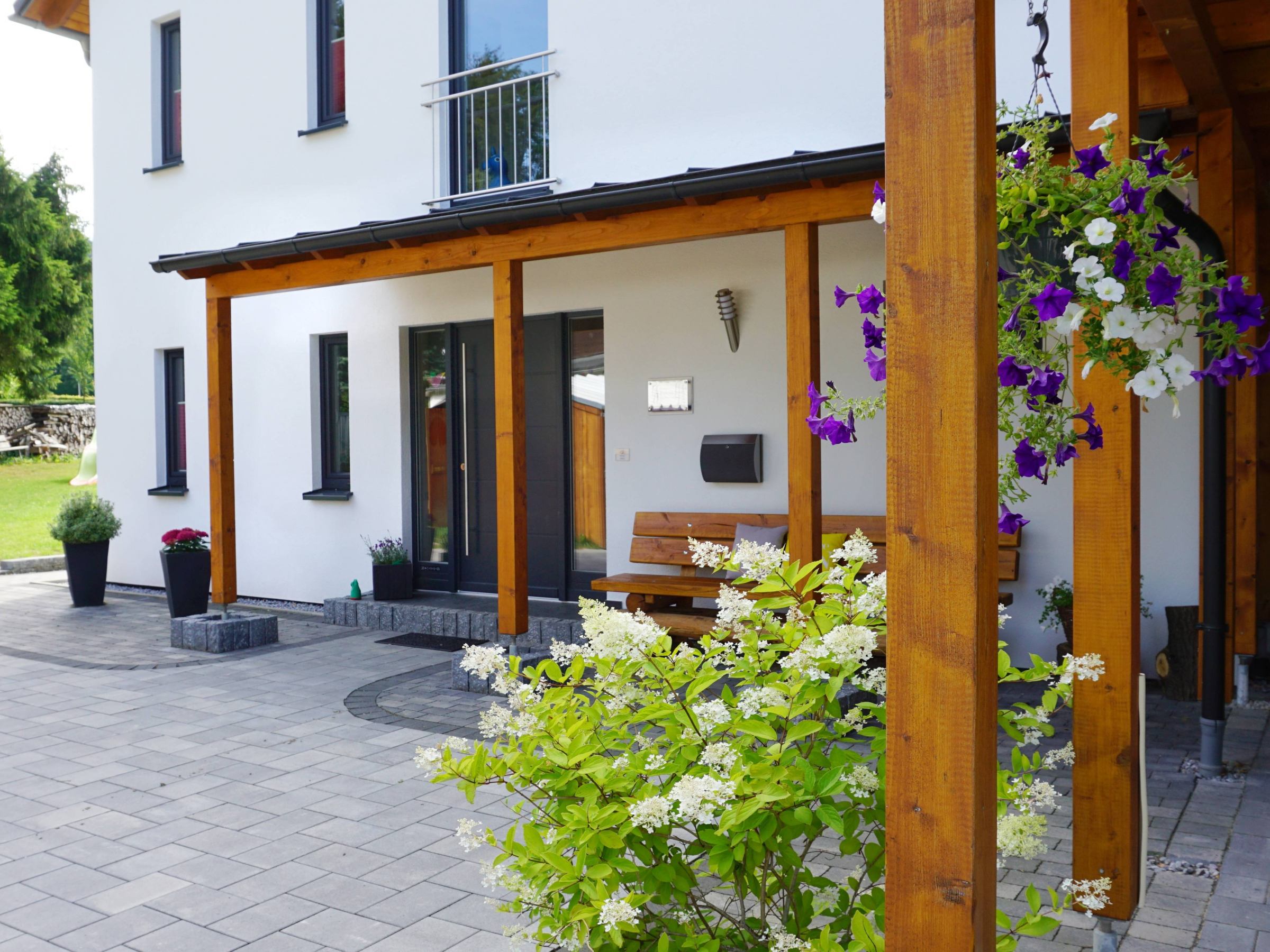 Überdachter Eingangsbereich eines Holzhauses mit sichtbaren Holzstützen und moderner Haustür