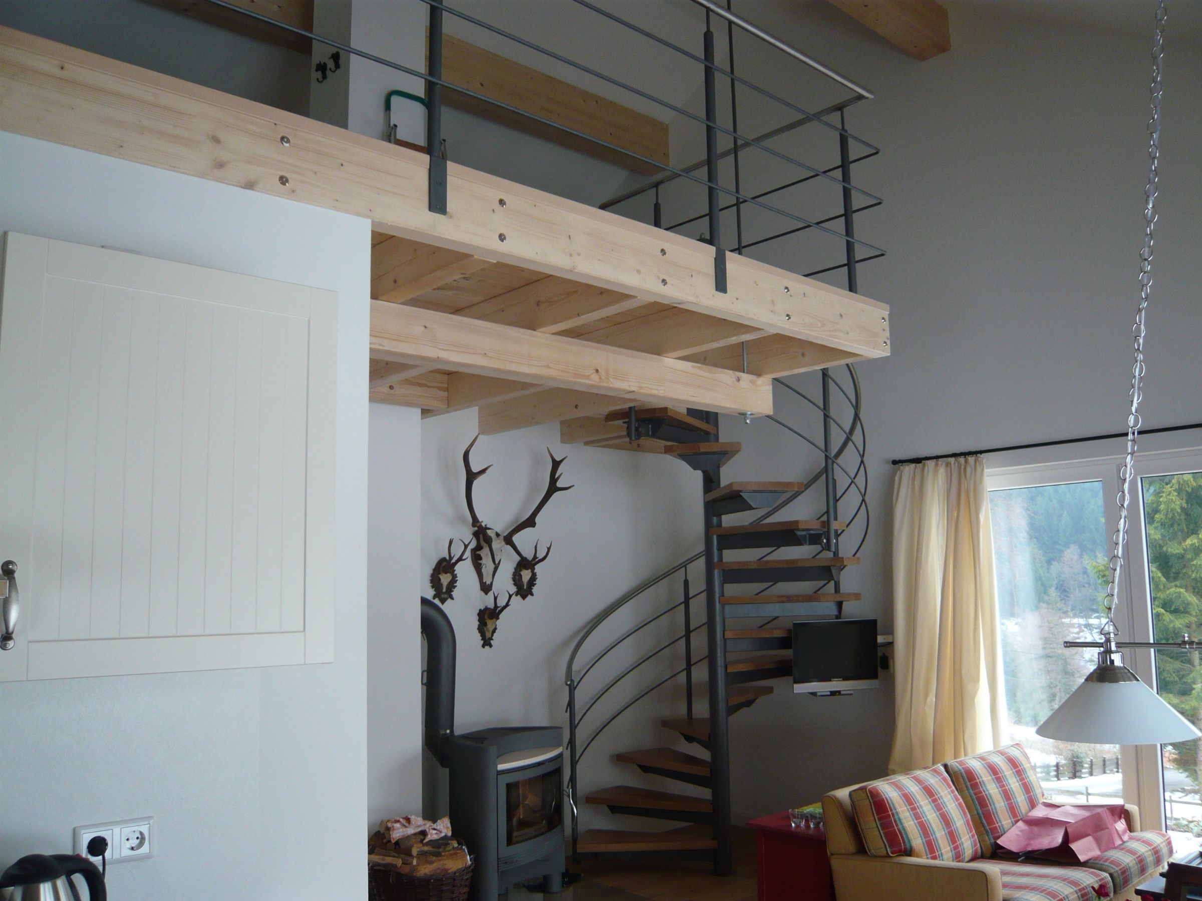 Blick von der Empore auf den Wohnraum mit sichtbarer Holzkonstruktion und Wendeltreppe
