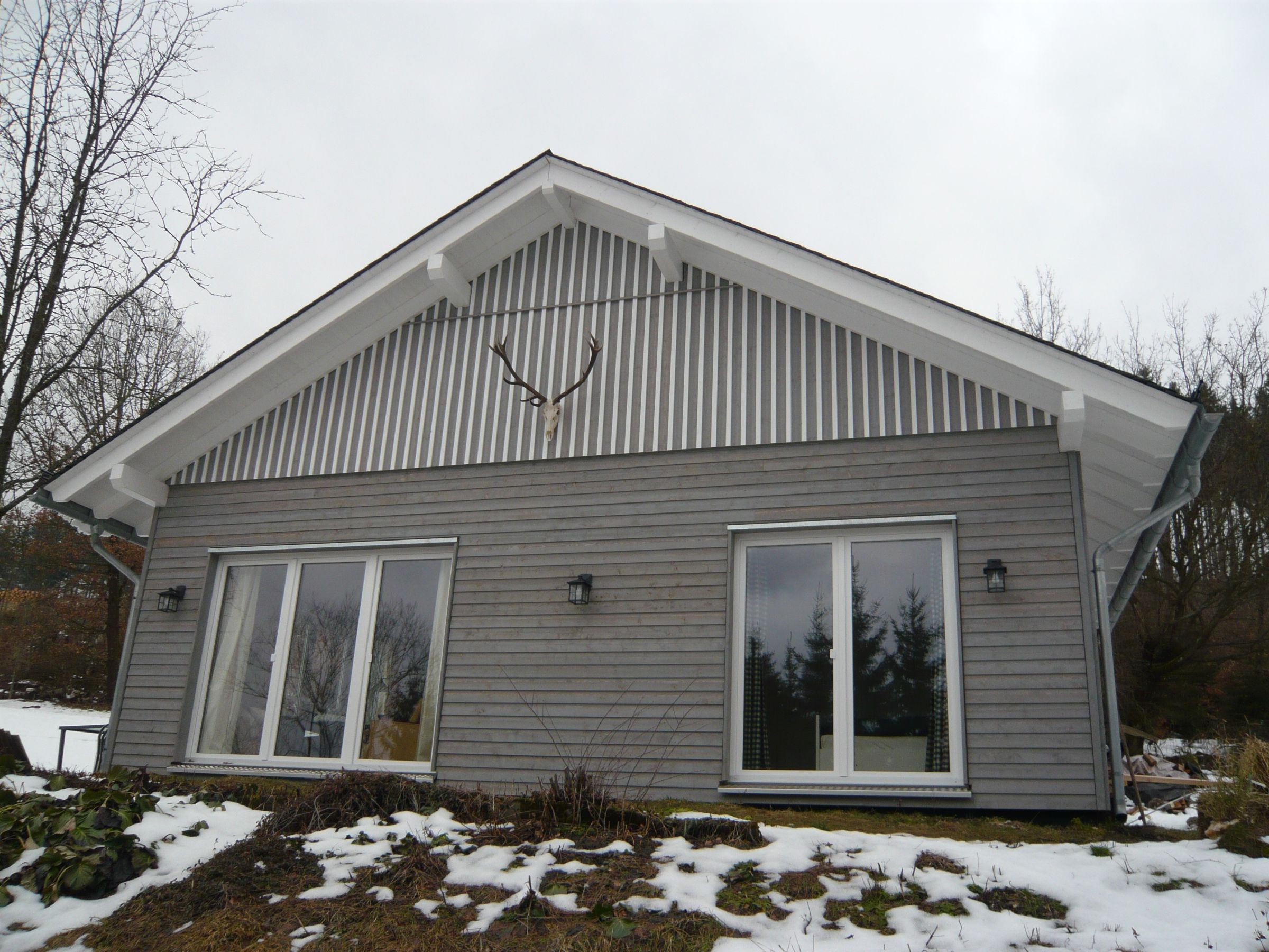 Giebelansicht eines Ferienhauses mit grauer Holzfassade und weißem Giebel im Winter