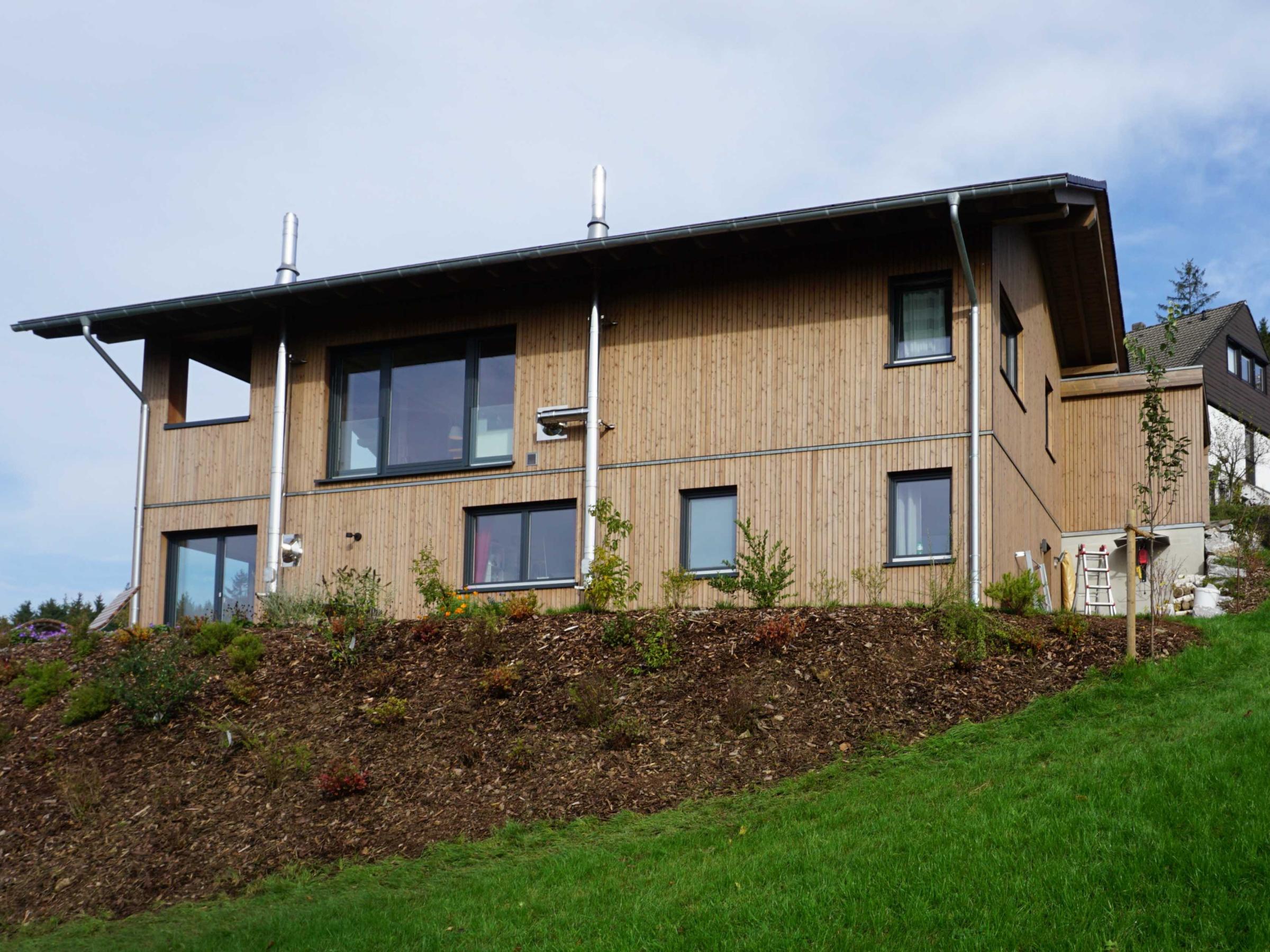 Seitenansicht des Hauses mit Holzfassade, großen Fenstern und Seitenblick auf den überdachten Balkon