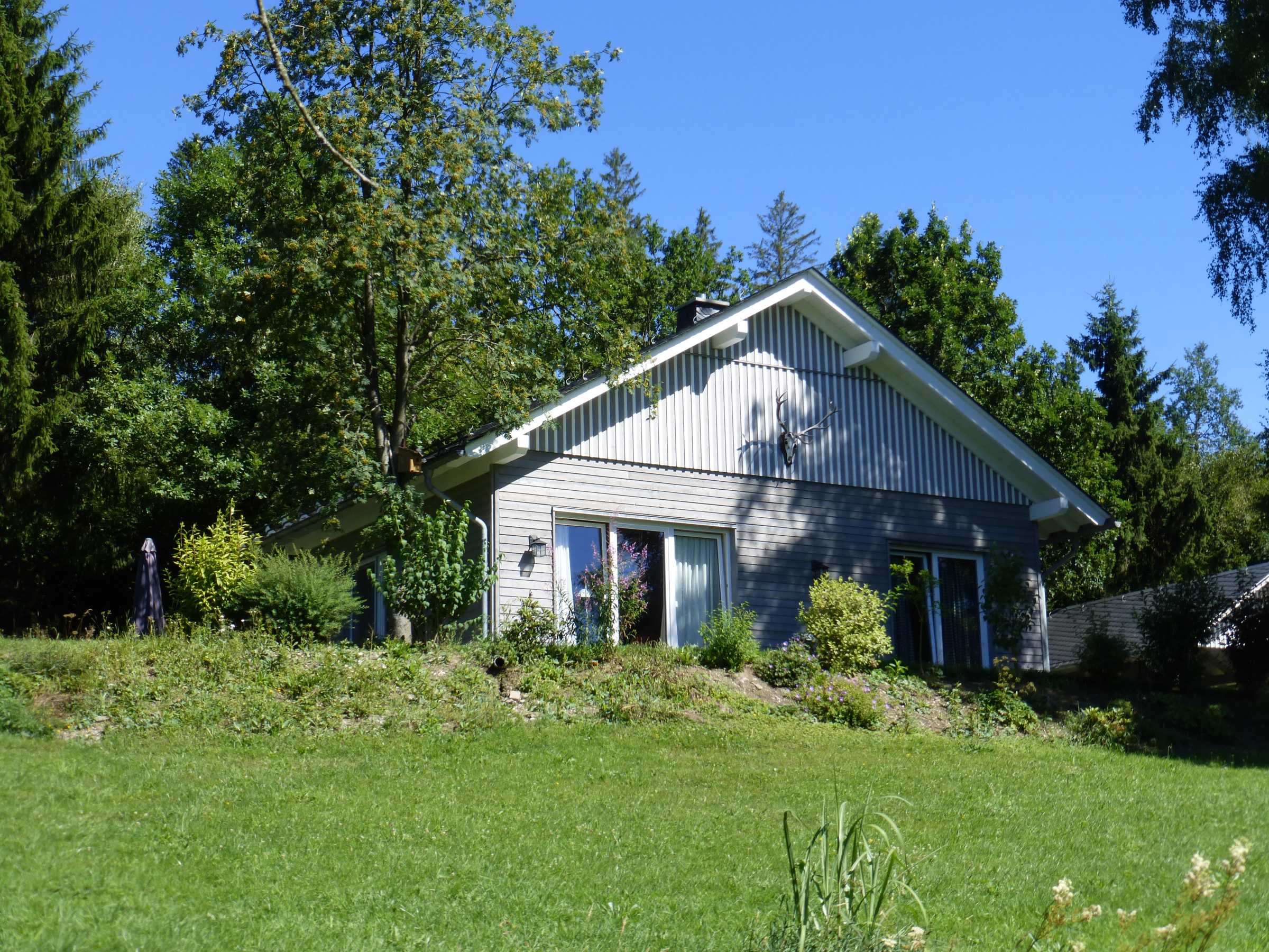 Ferienhaus in Holzrahmenbauweise mit grauer Holzfassade in sommerlicher Gartenlage