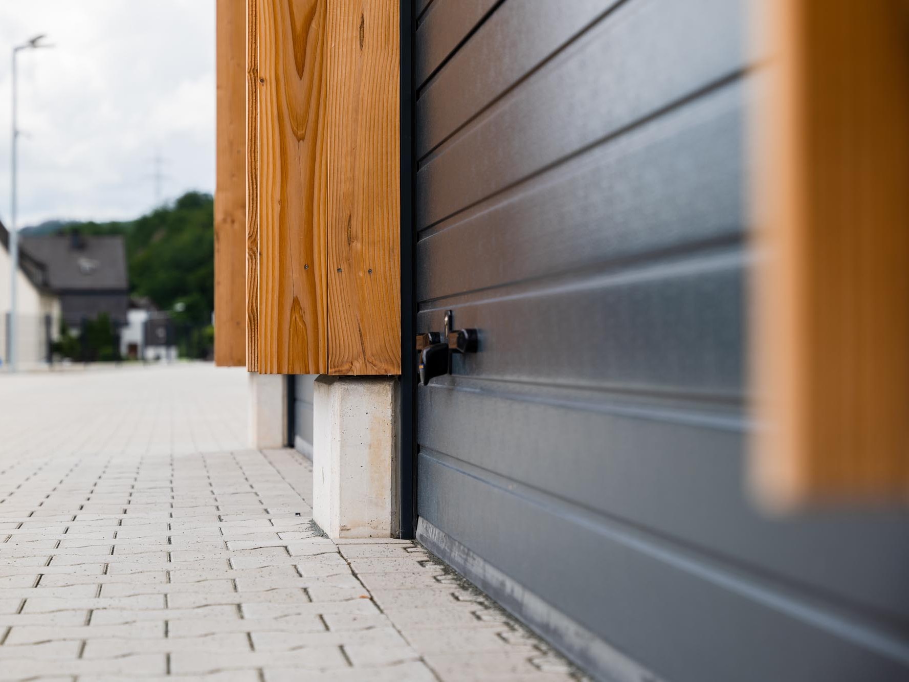 Detailansicht des Sockelanschlusses mit Holzstütze, Betonfundament und geschlossenem Garagentor