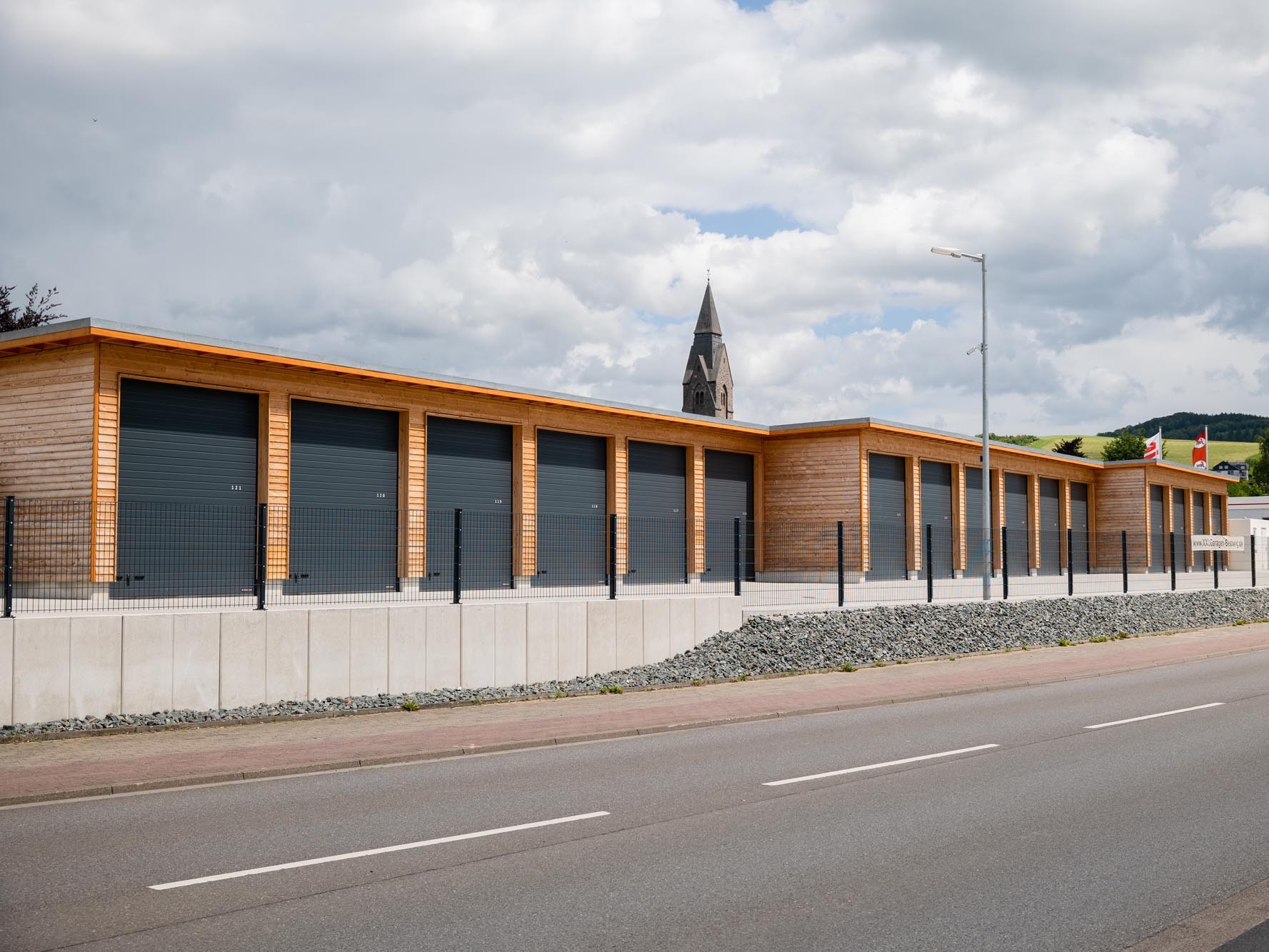 Straßenseitige Gesamtansicht eines Garagengebäudes mit Holzfassade und eingezäuntem Grundstück