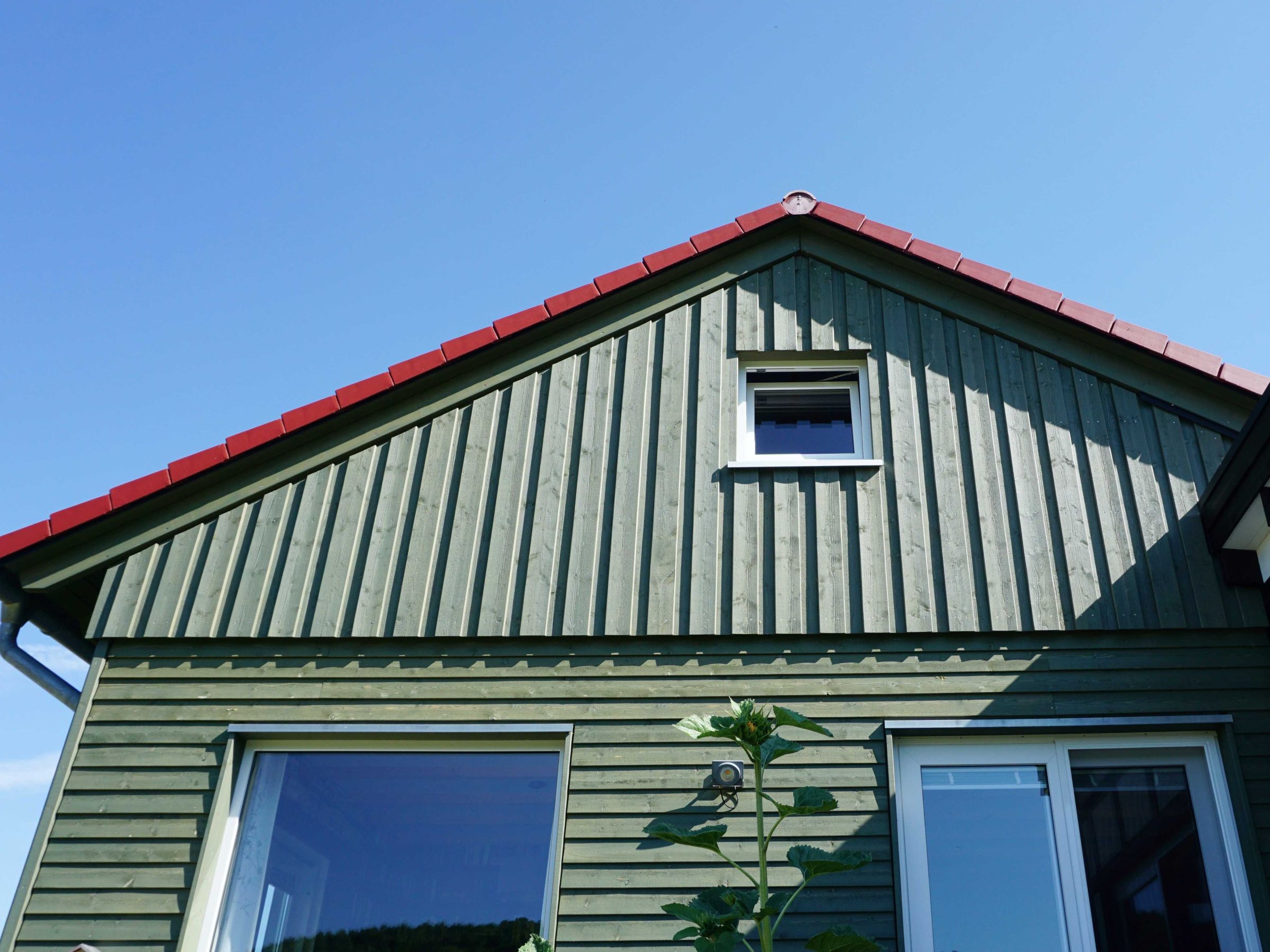 Giebelseite mit grüner Holzschalung, kleinem Fenster und geneigtem Dach mit roter Eindeckung