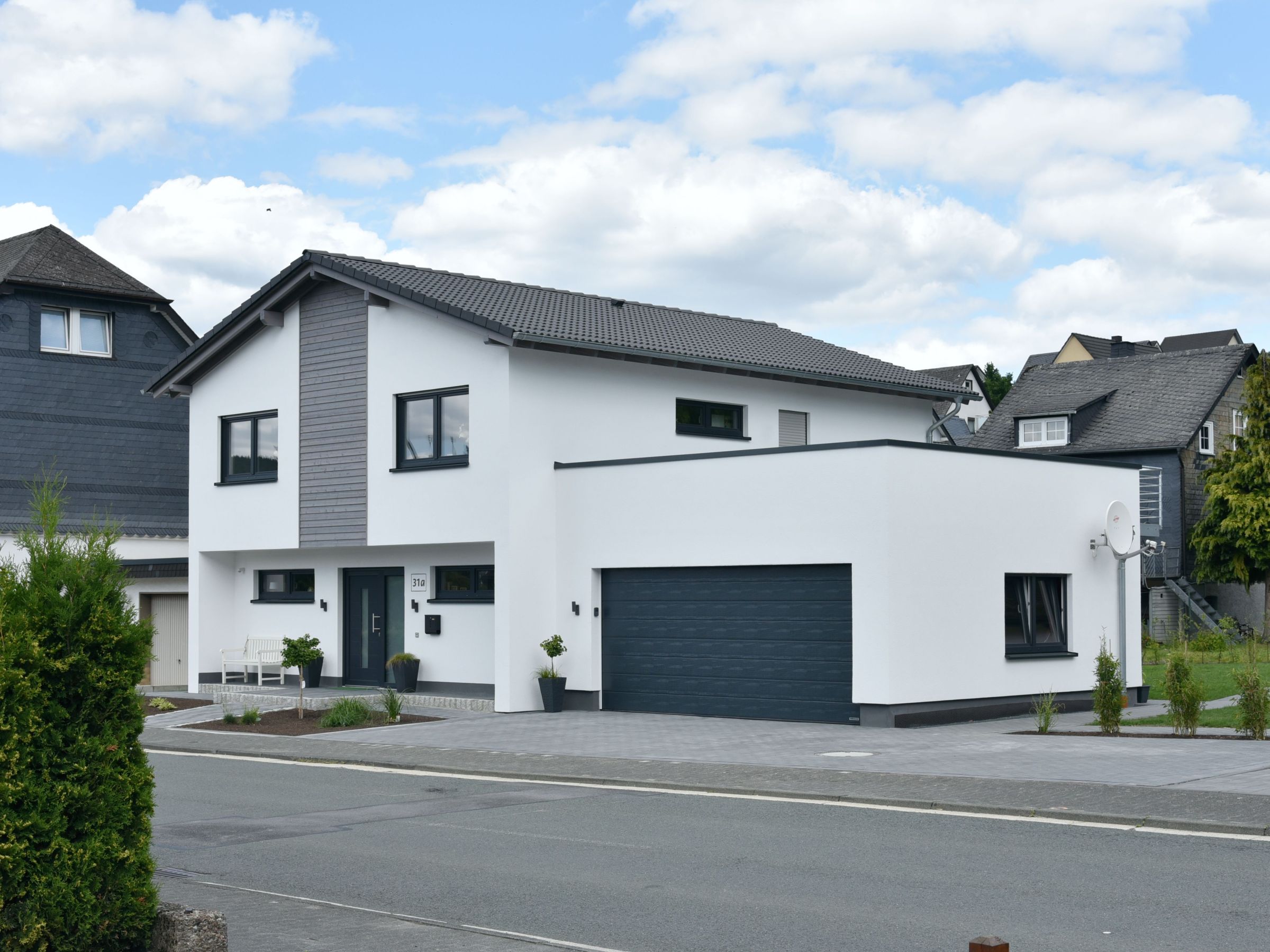 Außenansicht Haus Nübold-Bracht mit weißer Putzfassade, mittigem Holzfassadenstreifen und integrierter Satteldach-Garage