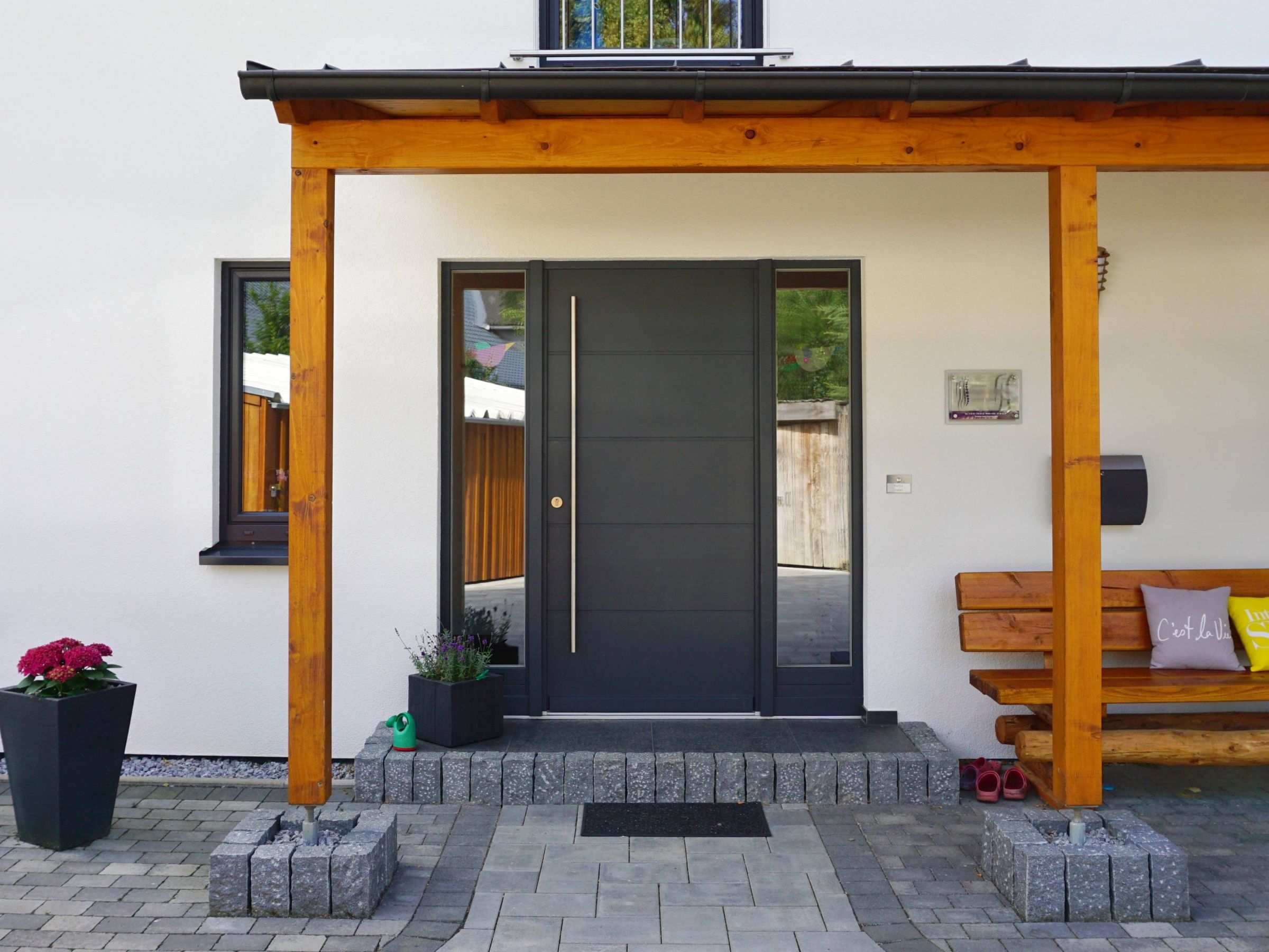 Moderne Haustür eines Einfamilienhauses unter Holzvordach mit klarer Fassadengestaltung