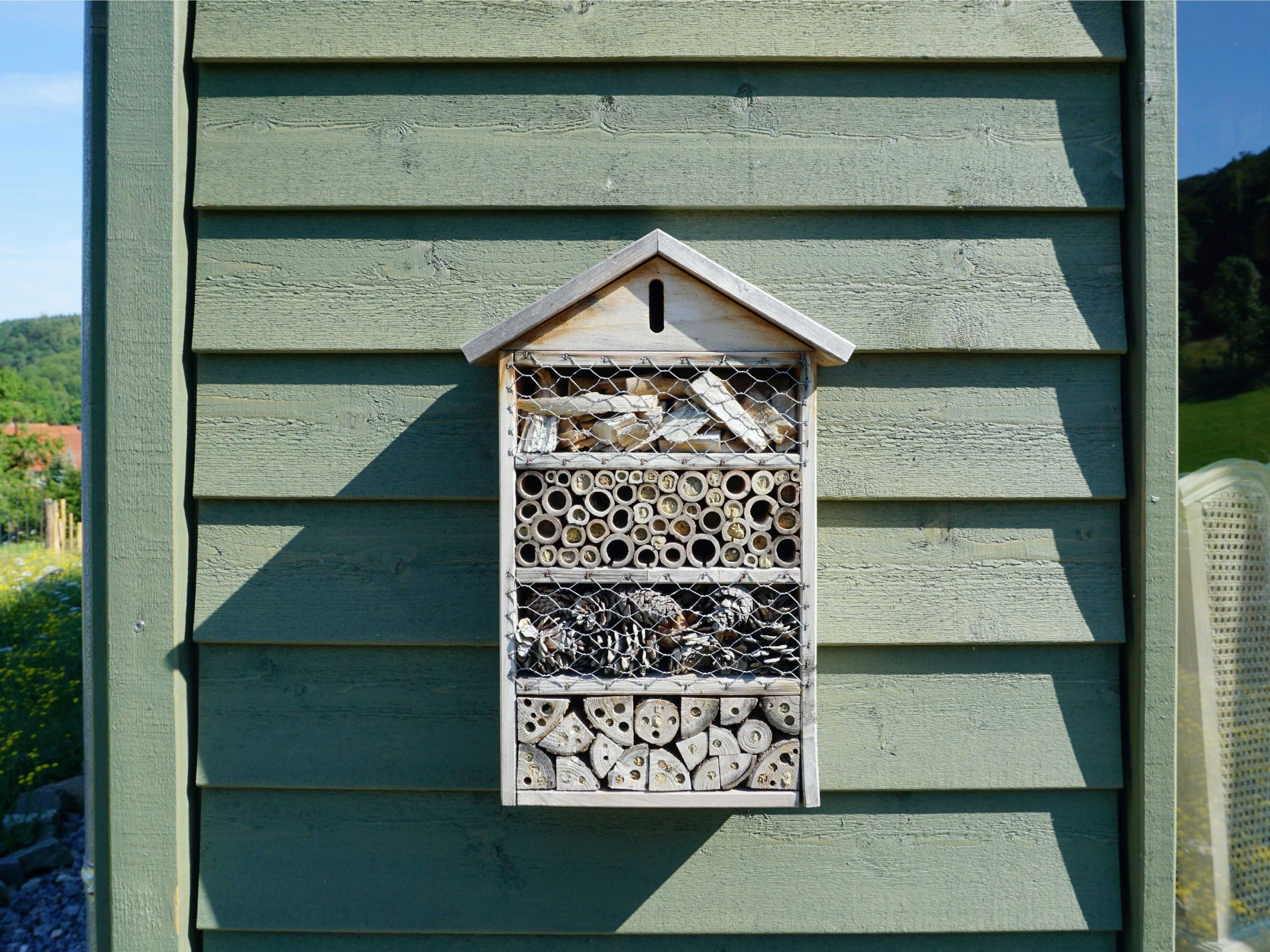 Insektenhotel an der grünen Holzfassade des Hauses als Detail der naturnahen Gestaltung