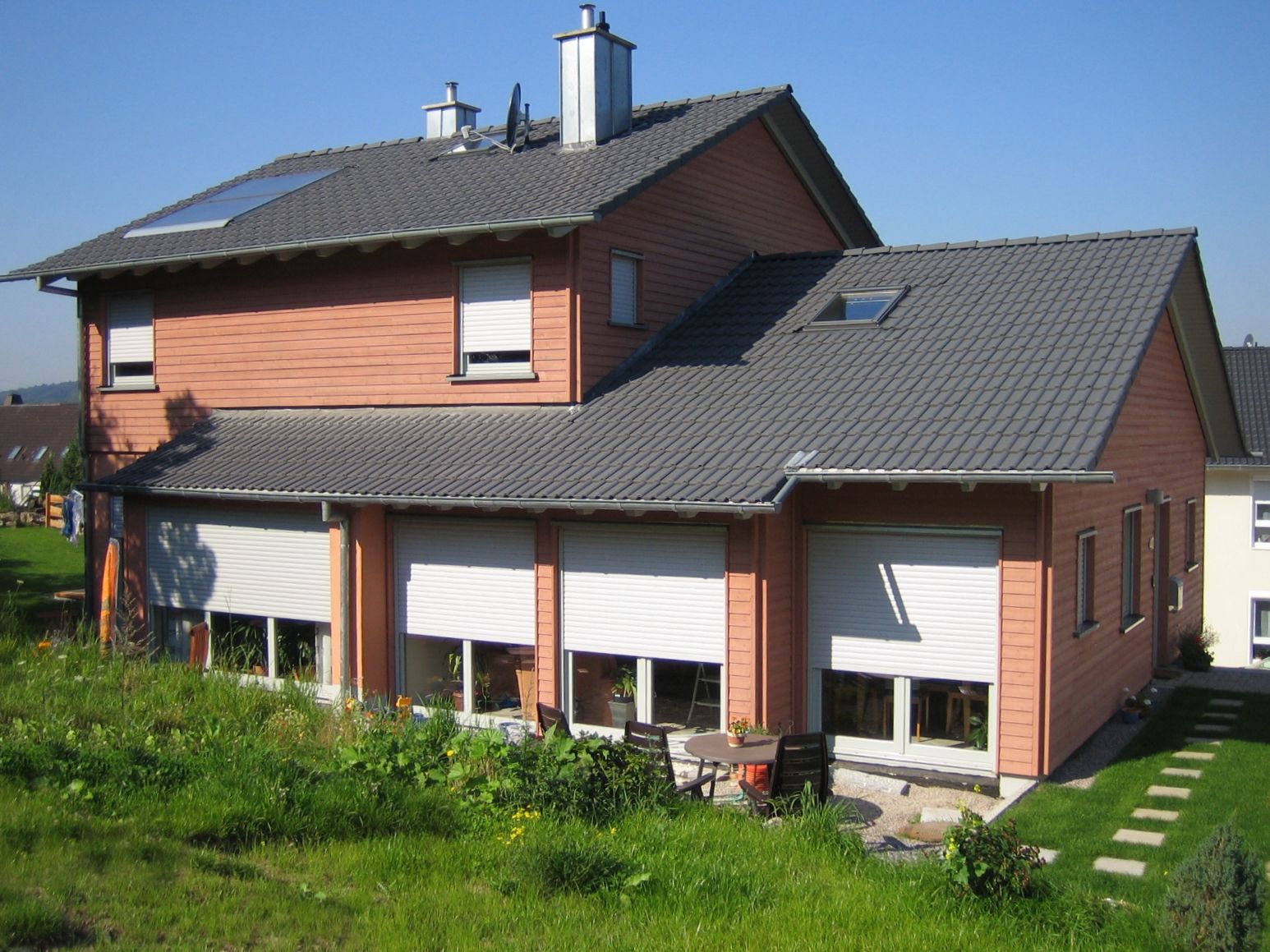 Mehrfamilienhaus mit terracottafarbener Holz- und Putzfassade in Hanglage