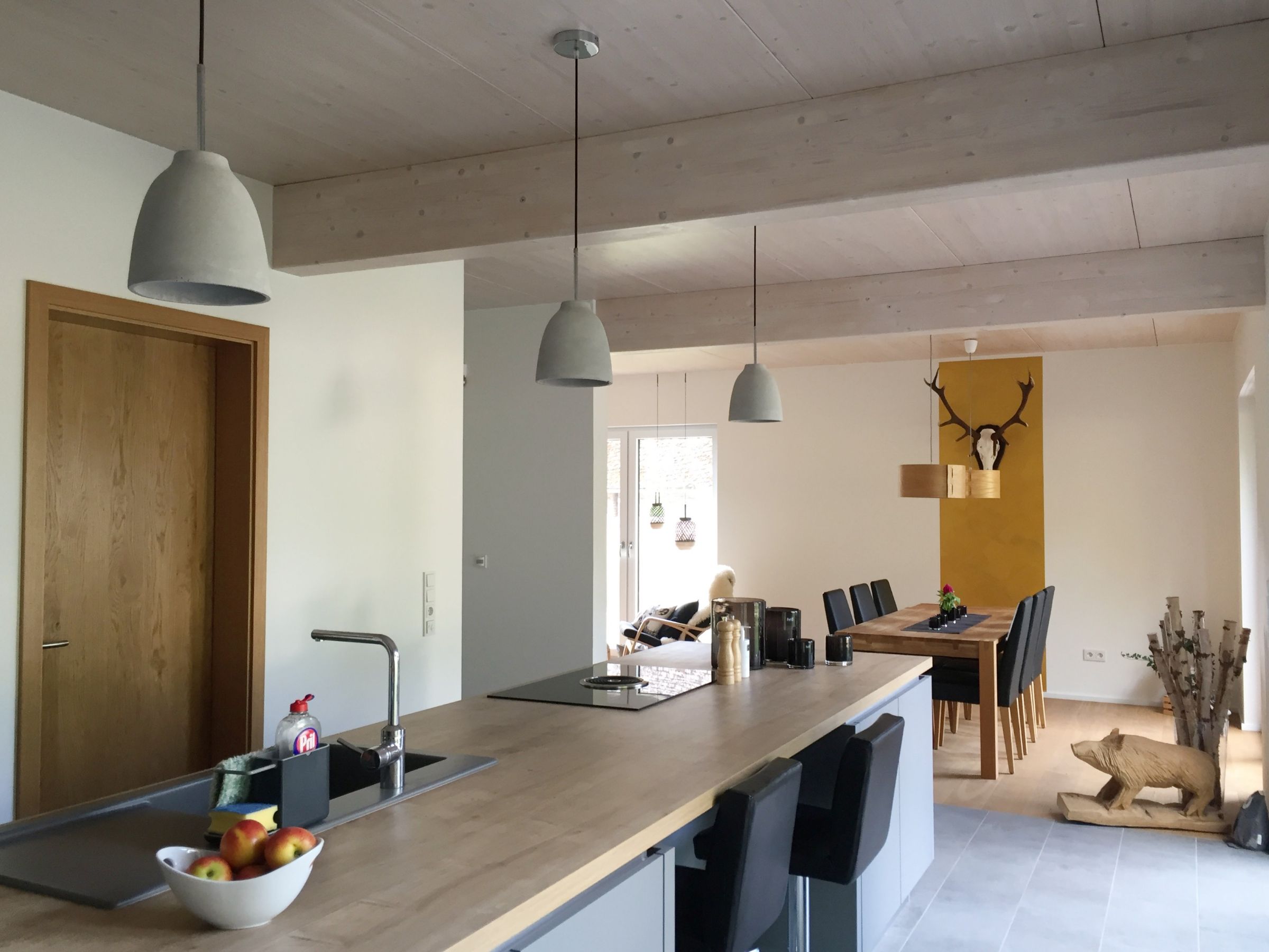 Offene Küche mit Kochinsel und sichtbarer Massivholzdecke im Holzhaus