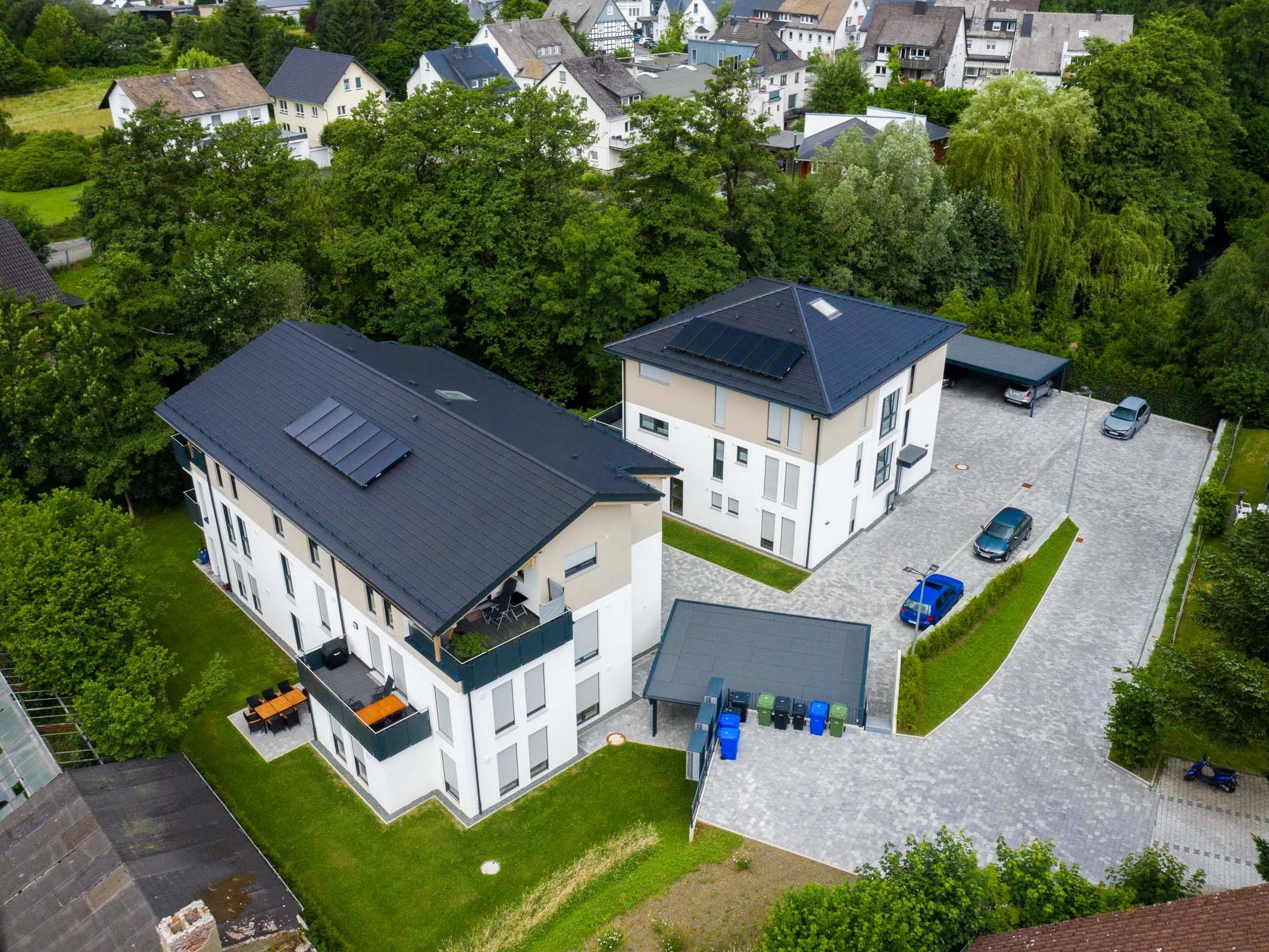 Luftaufnahme von zwei Mehrfamilienhäusern mit Außenanlagen, Stellplätzen und Carports