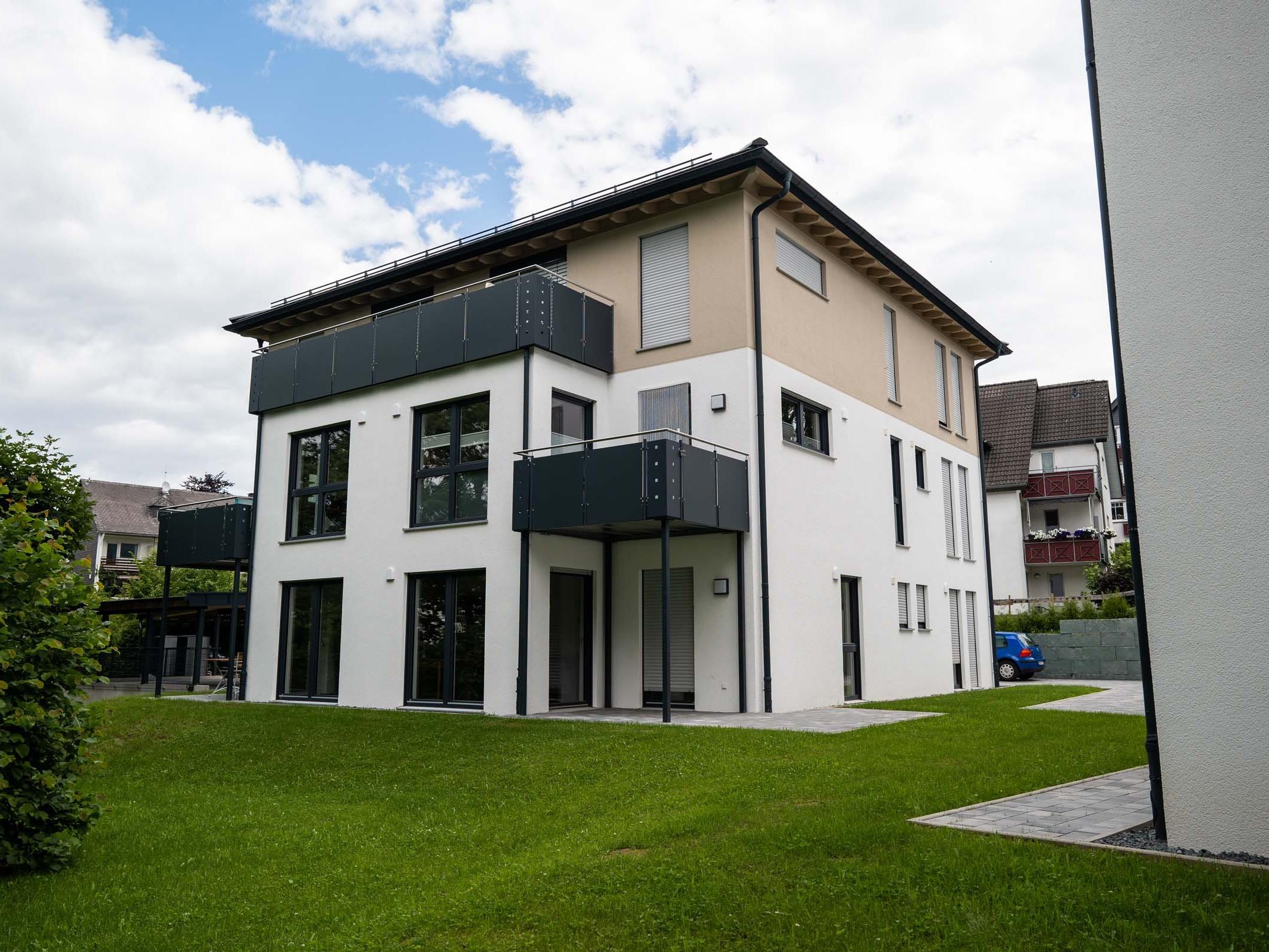 Gartenansicht eines Mehrfamilienhauses mit Balkonen, hohen Fenstern und Grünfläche