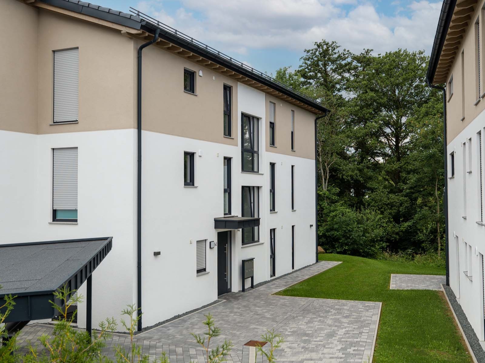 Hofbereich zwischen den Baukörpern mit Pflasterung, Eingangszone und Baumbestand