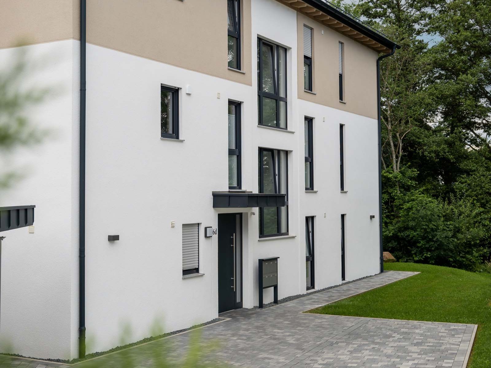 Eingangsbereich des Mehrfamilienhauses mit Vordach, zweifarbiger Putzfassade und vertikaler Fensterfläche