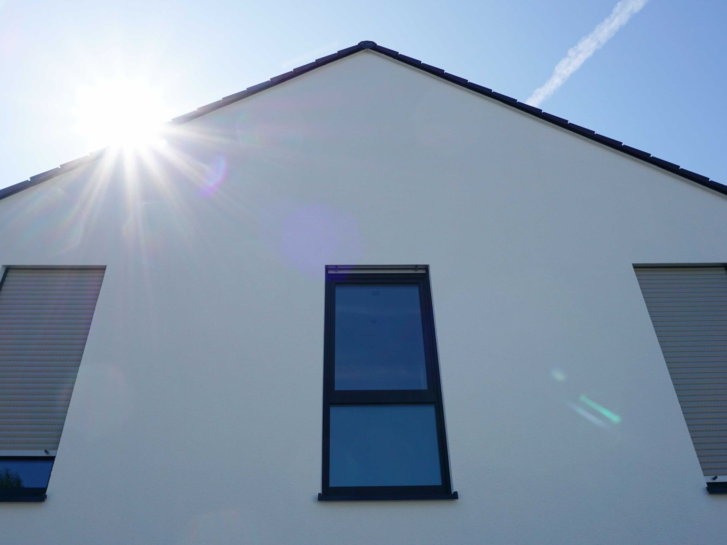 Giebelfassade eines Mehrfamilienhauses mit weißer Putzfassade und stehenden Fenstern