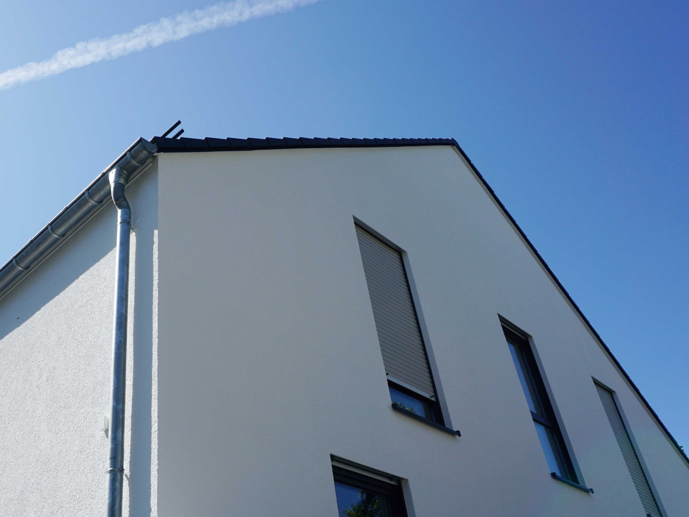 Seitenansicht eines Mehrfamilienhauses mit weißer Fassade und geschlossenem Dachrand