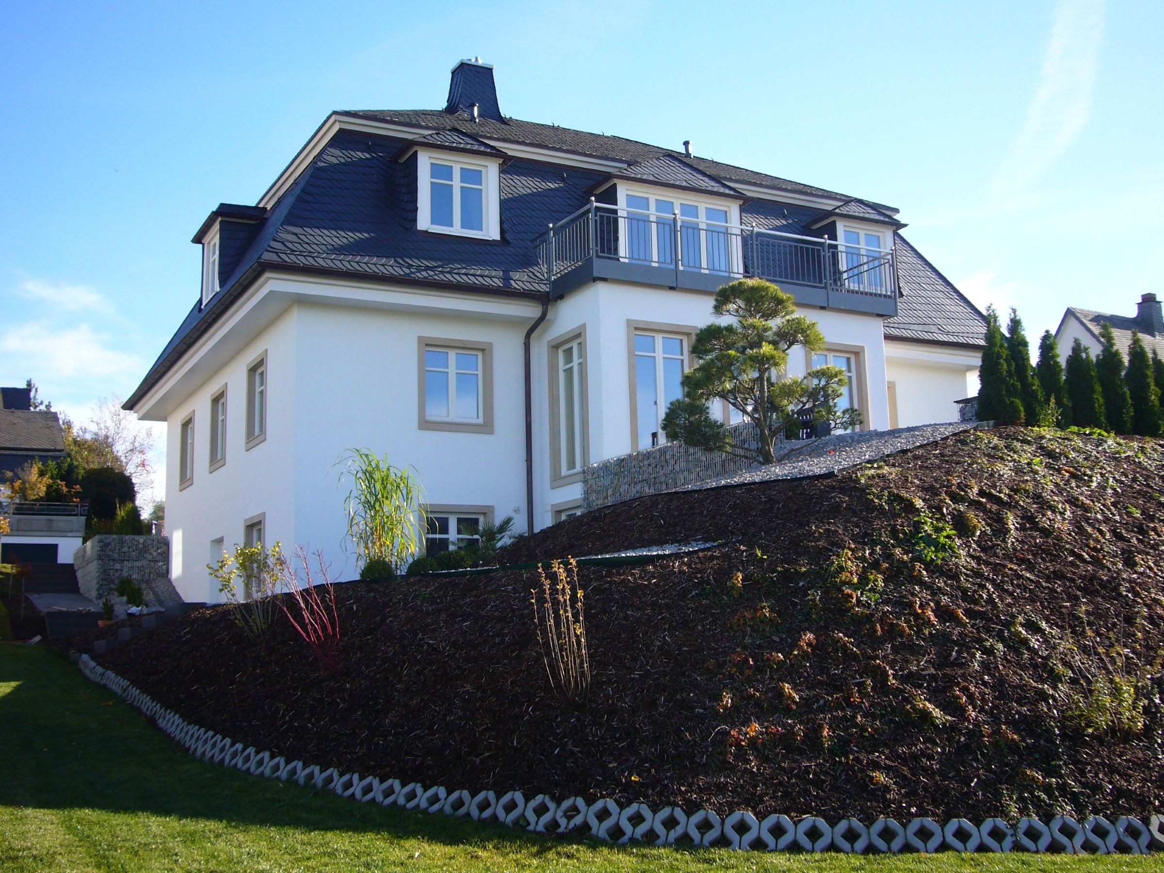 Einfamilienhaus mit Mansarddach und Balkon in Hanglage von der Gartenseite