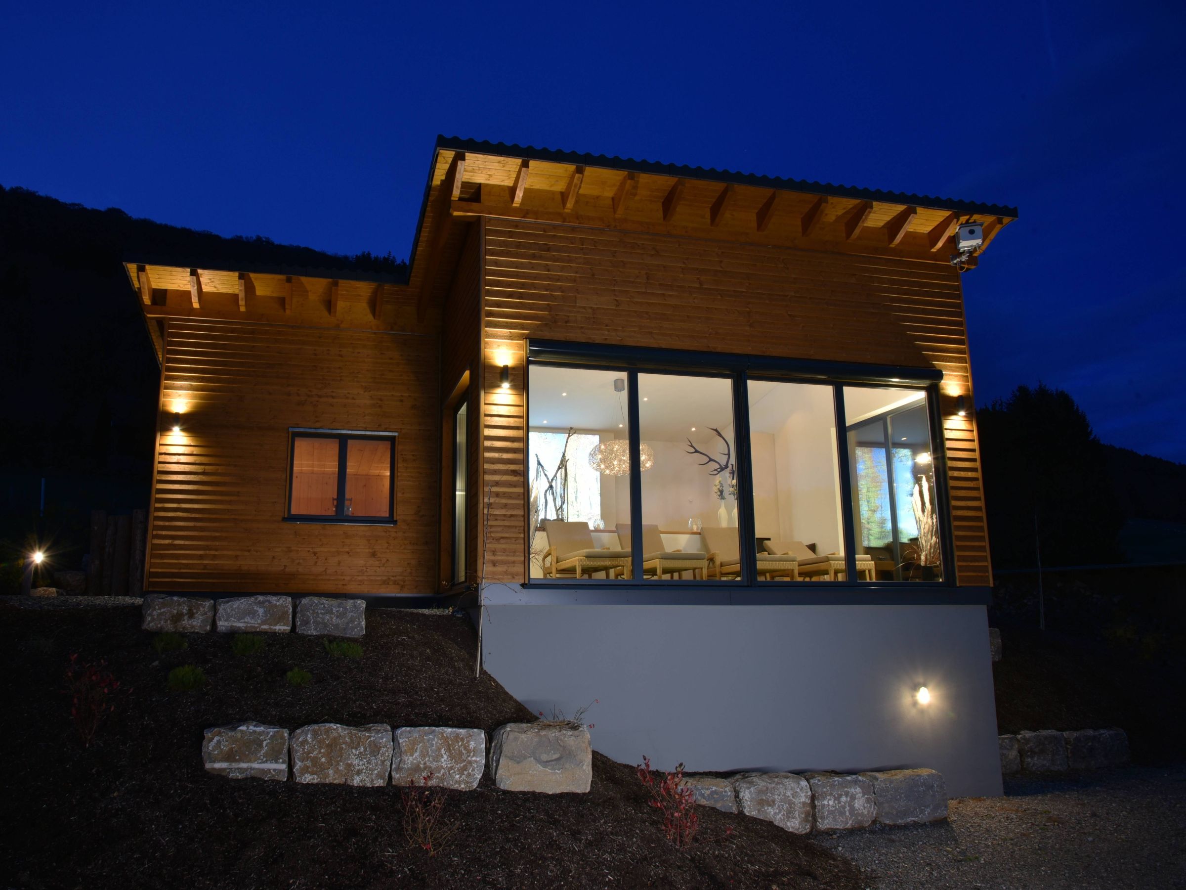 Saunahaus bei Dämmerung mit beleuchtetem Innenraum und Holzfassade