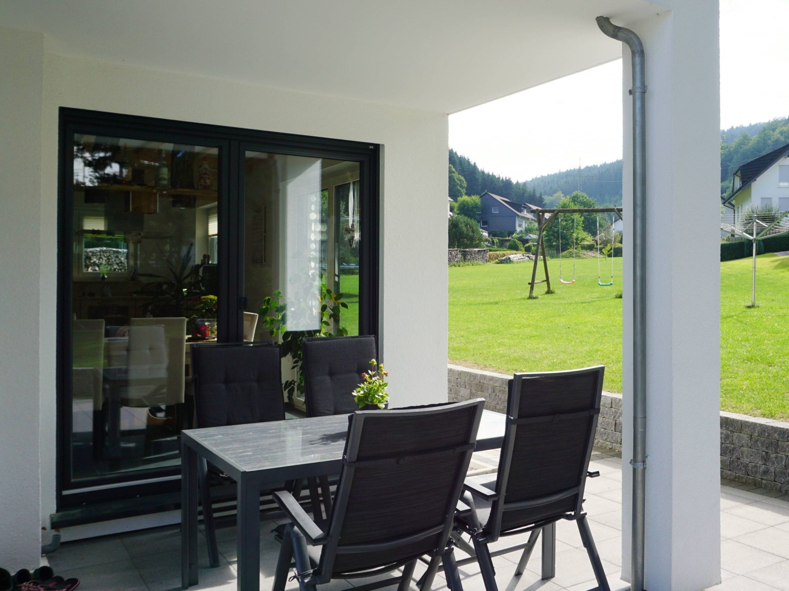 Überdachte Terrasse mit Sitzplatz und bodentiefen Fenstern im Erdgeschoss eines Holzhauses