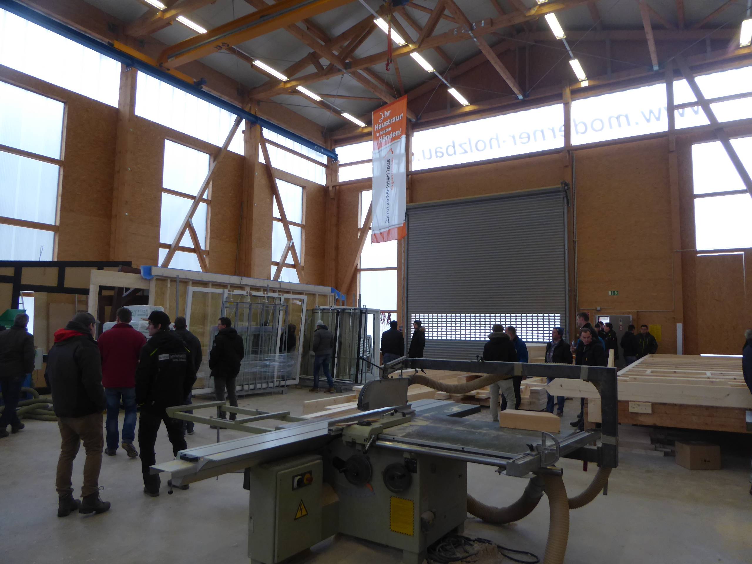 Gruppe von Besuchern bewegt sich durch eine Produktionshalle mit Maschinen und Holzelementen