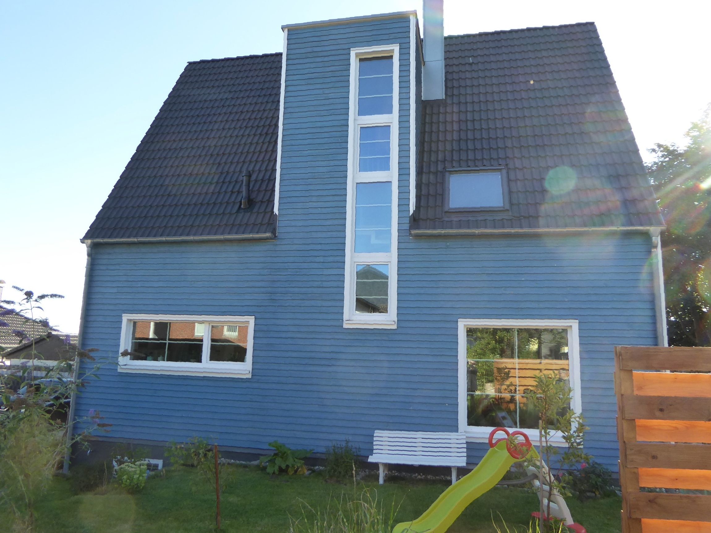 Rückansicht eines friesenblauen Holzhauses mit Garten und Satteldach