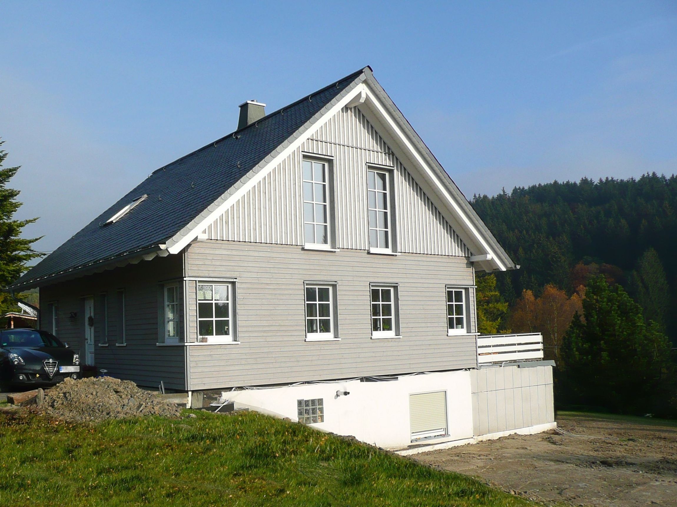 Rückseite eines Holzhauses mit sichtbarem Bestandskeller und Hanglage