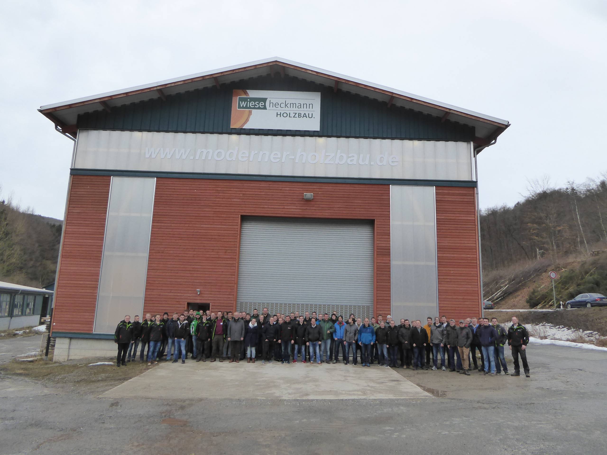 Große Besuchergruppe steht vor einer Holzbauhalle mit Firmenbeschriftung