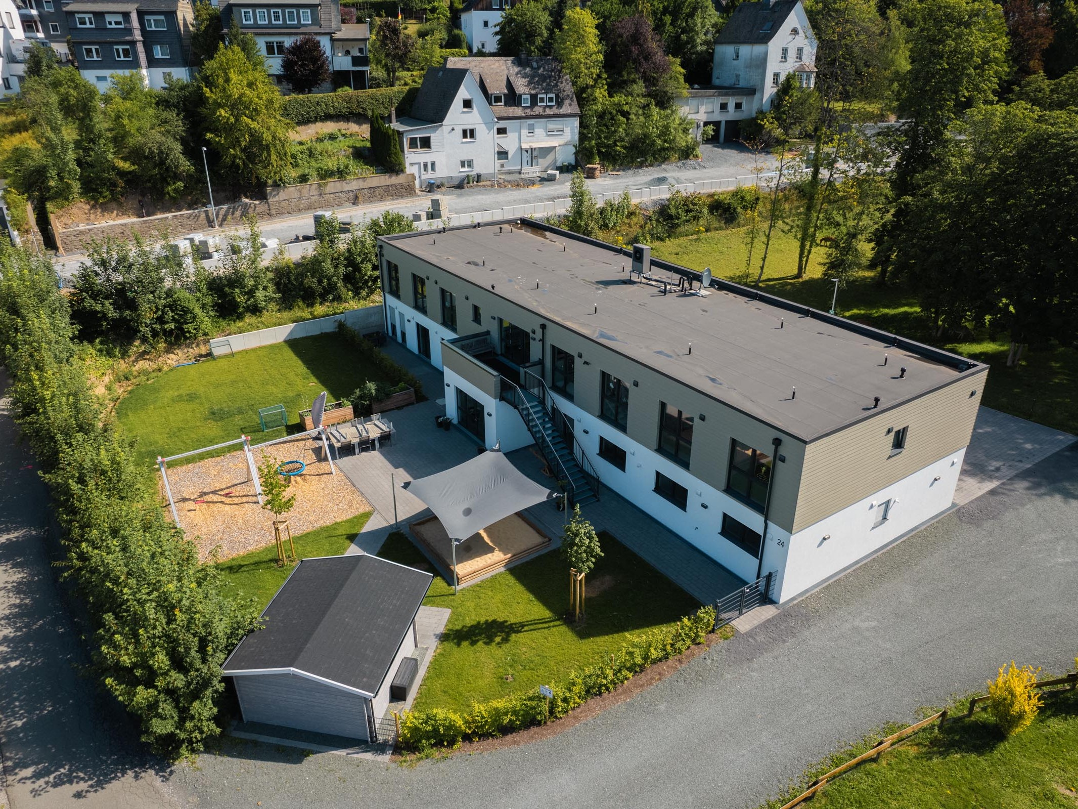 Luftaufnahme der Außenwohngruppe mit Außenanlagen, Spielbereich und Carport in Olsberg.